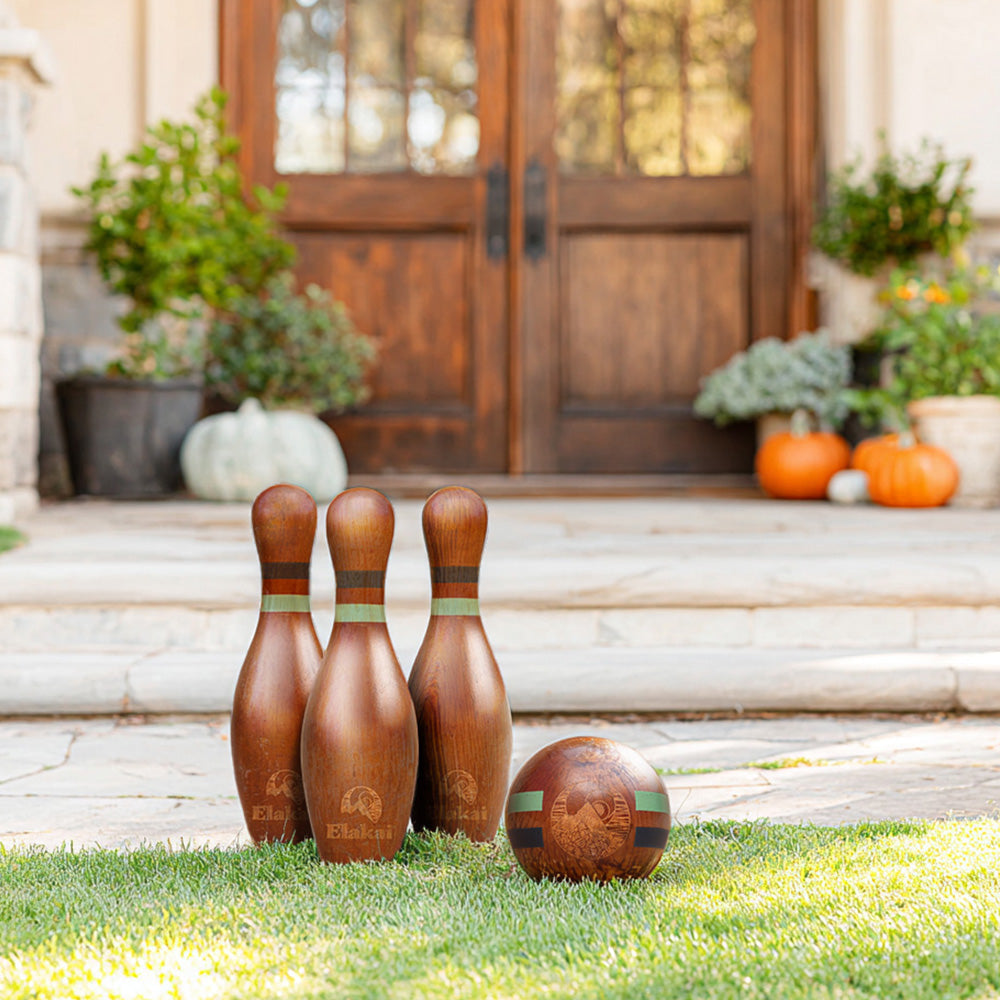 Wooden bowling pins and ball on grass in front of a house with pumpkins.