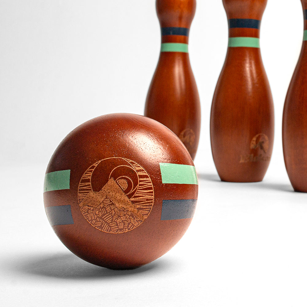 Wooden bowling ball with decorative patterns and three wooden pins on a white background