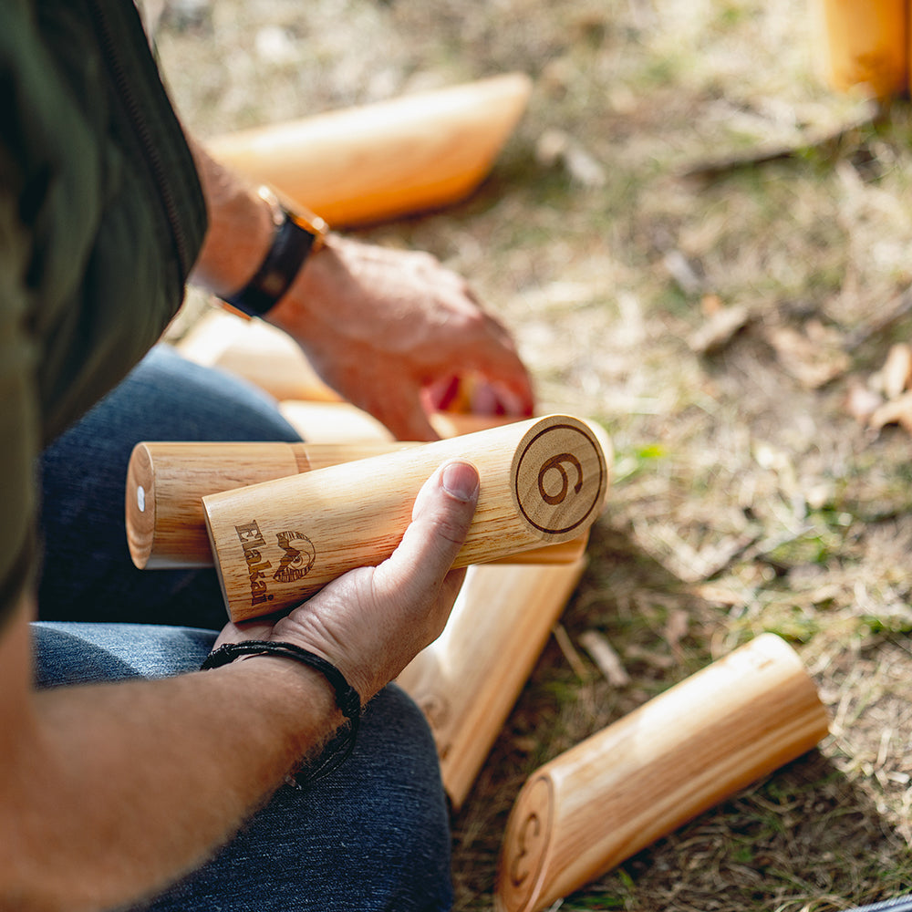 Person holding wooden kubb pieces with a blurred outdoor background