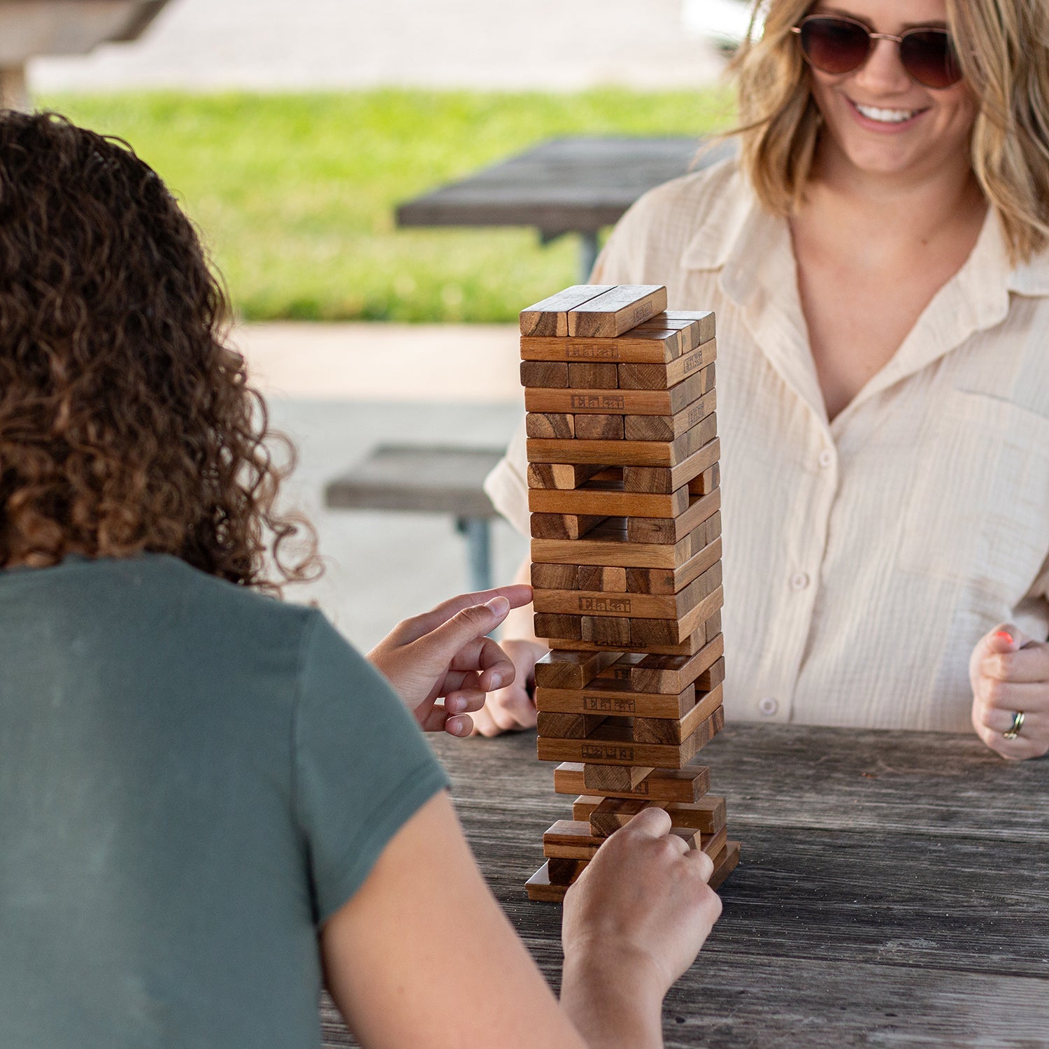 Two people playing Jenga outdoors on a wooden table.