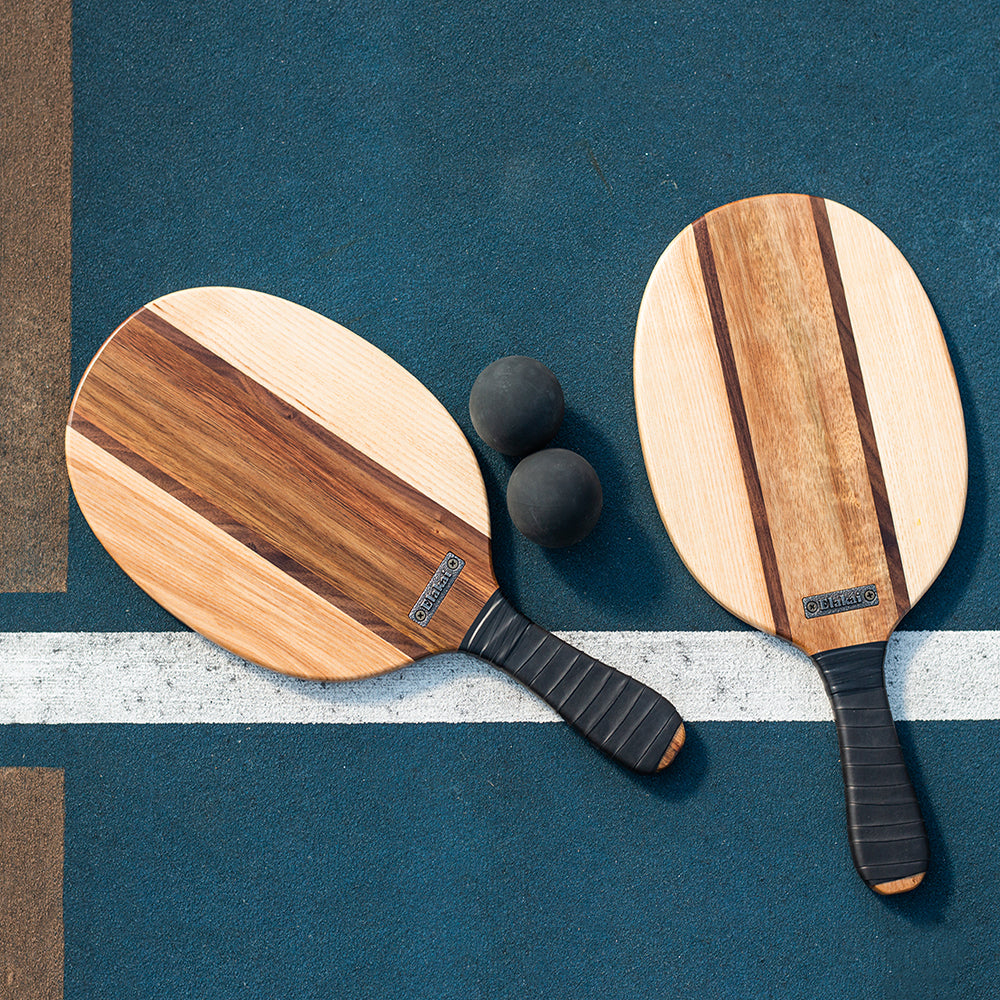 Two wooden paddle sports equipment with black balls on a blue background