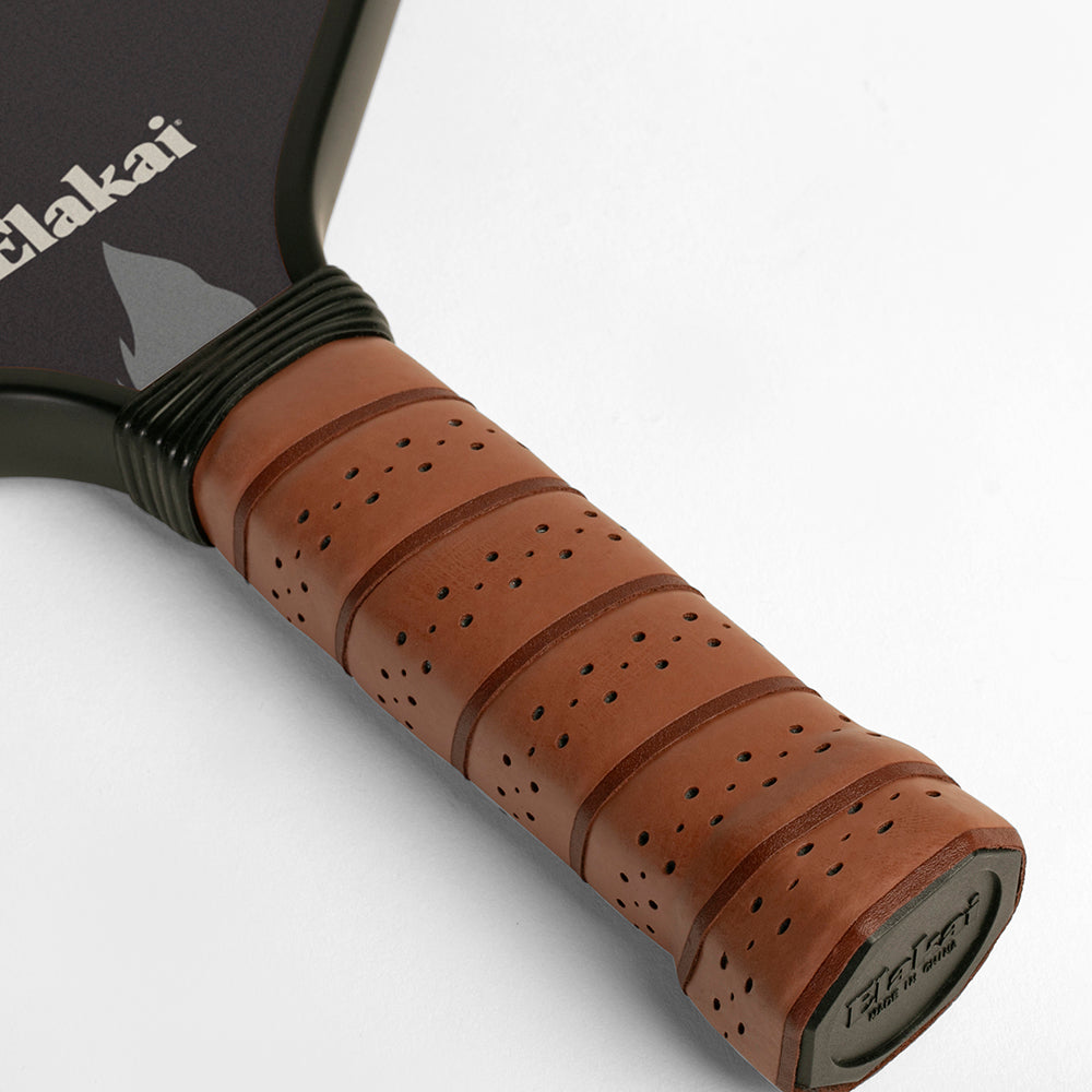 Close-up of a pickleball paddle handle with brown grip and black Elakai branding.