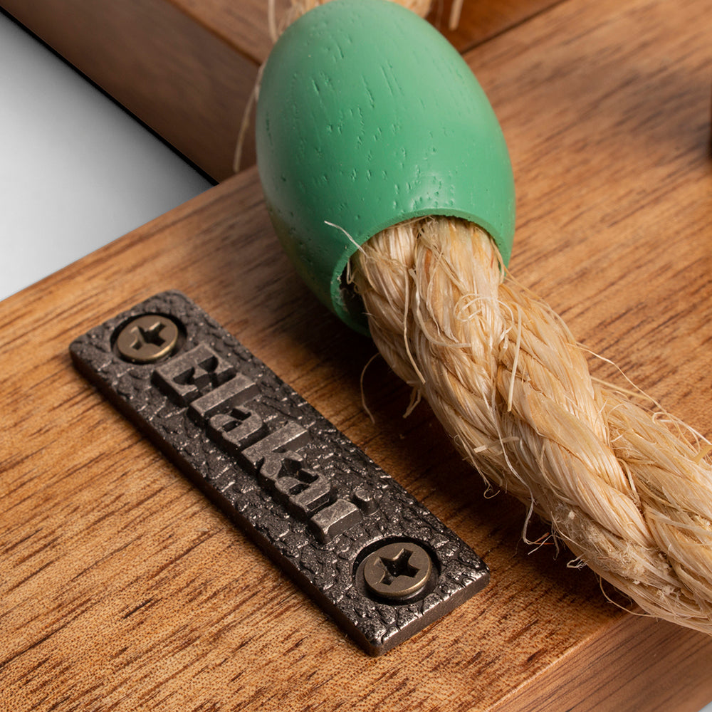 Green rubber dog toy with rope on a wooden surface, featuring a metal tag with 'Bella' engraved.