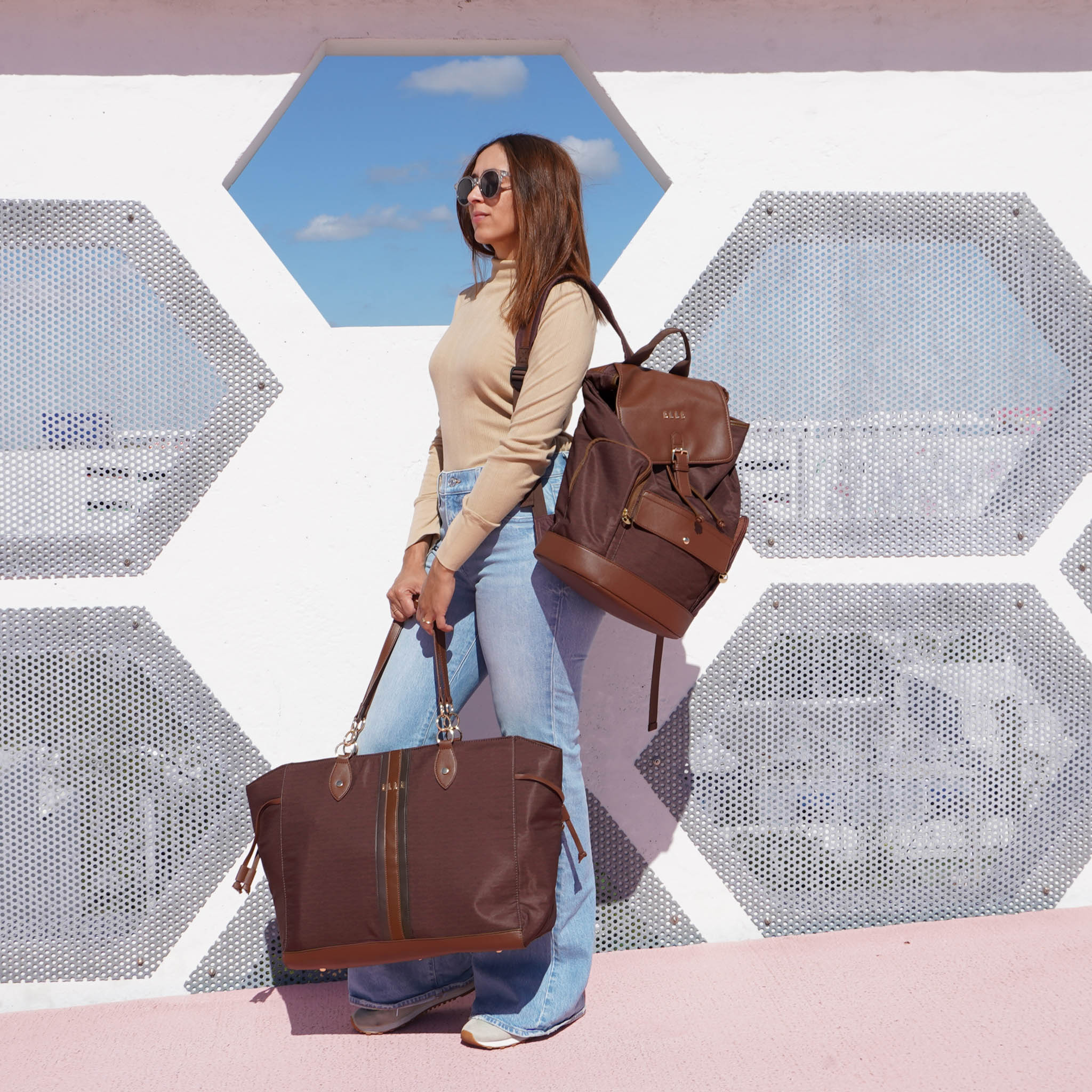 Woman holding two brown bags against a geometric wall with blue sky.