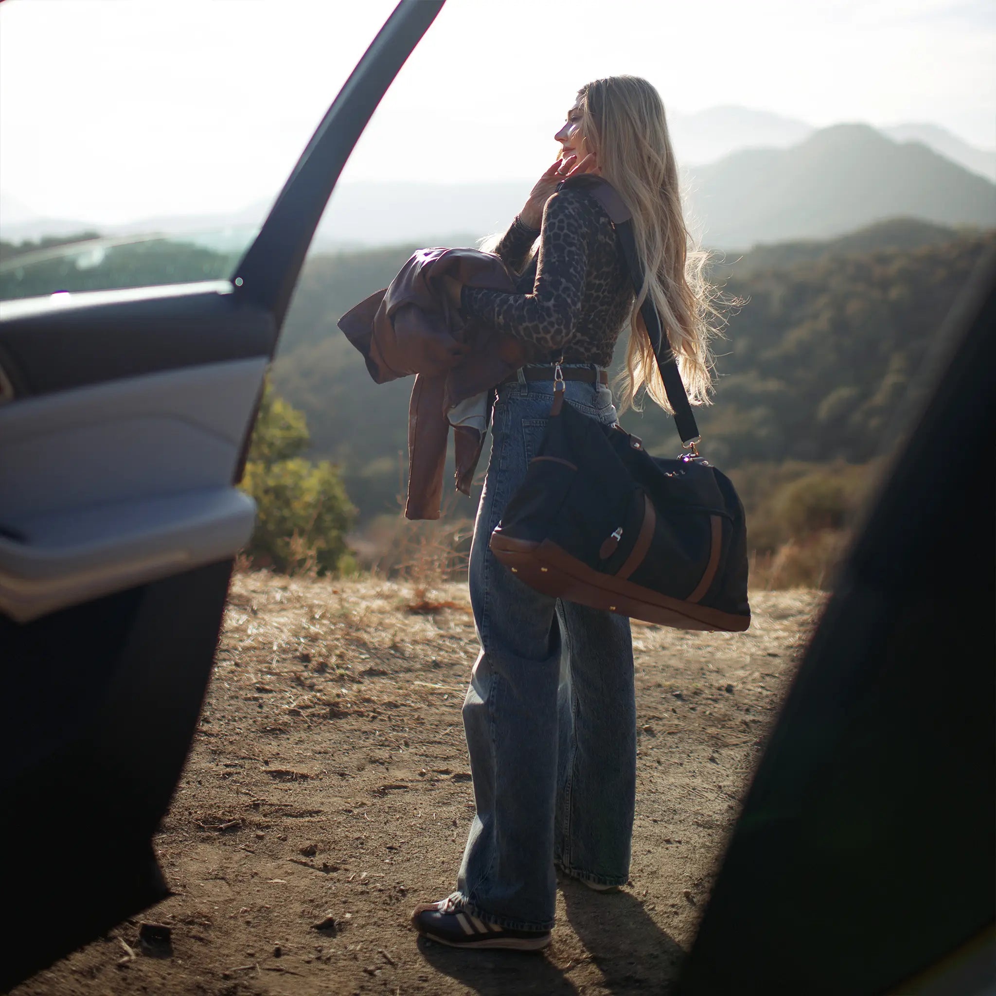 Woman standing next to an open car door with a scenic mountain view