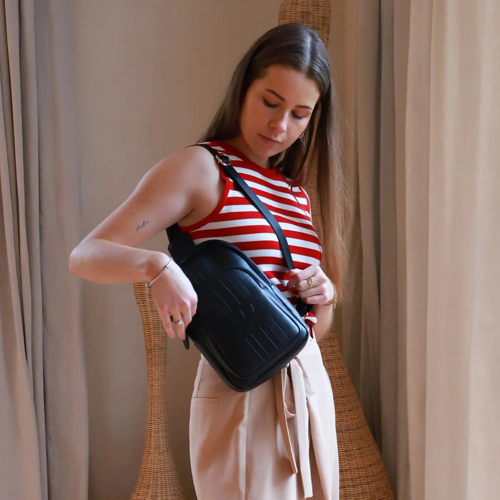 Woman holding a black bag in a room with beige curtains