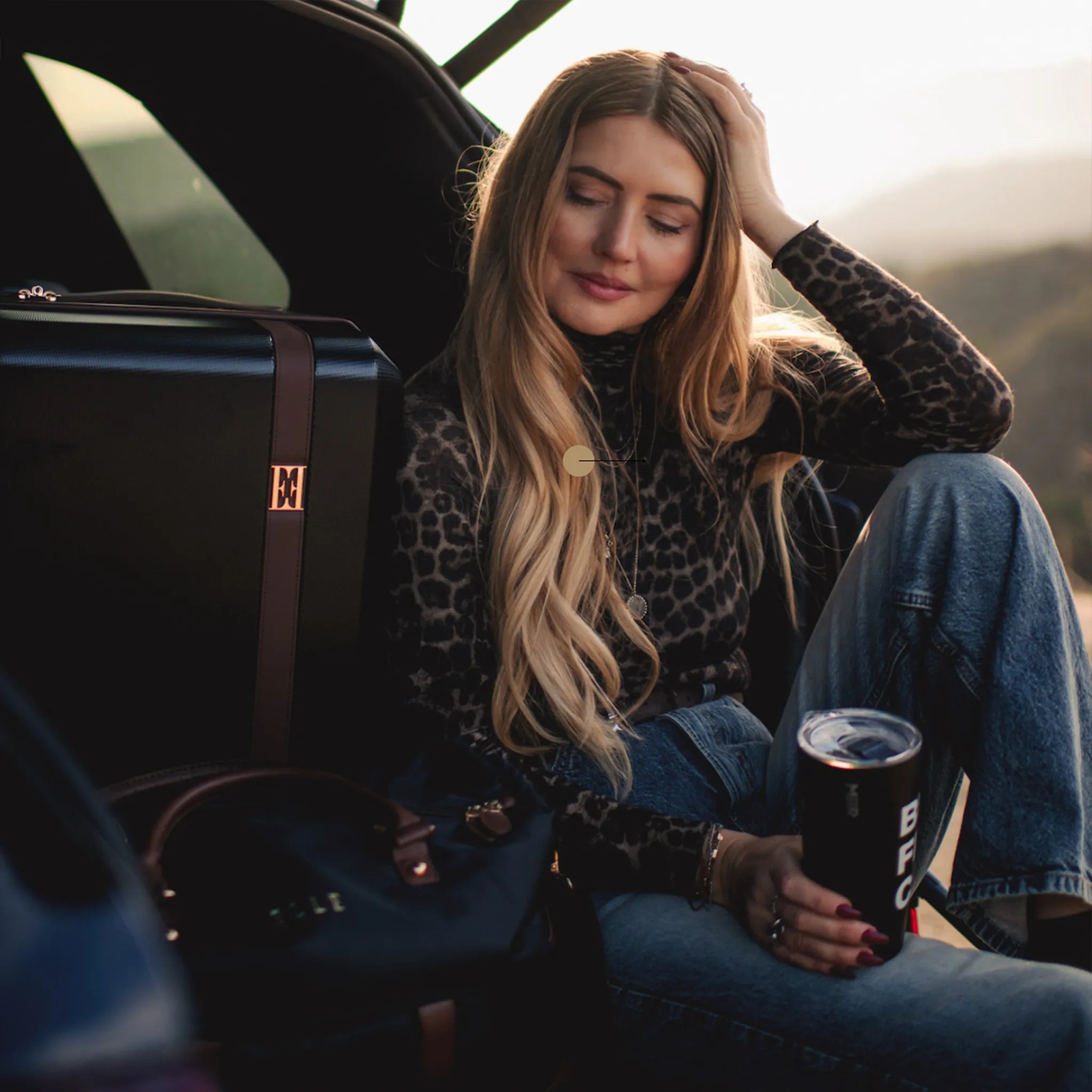Woman sitting in a car with a can of beer, surrounded by luggage