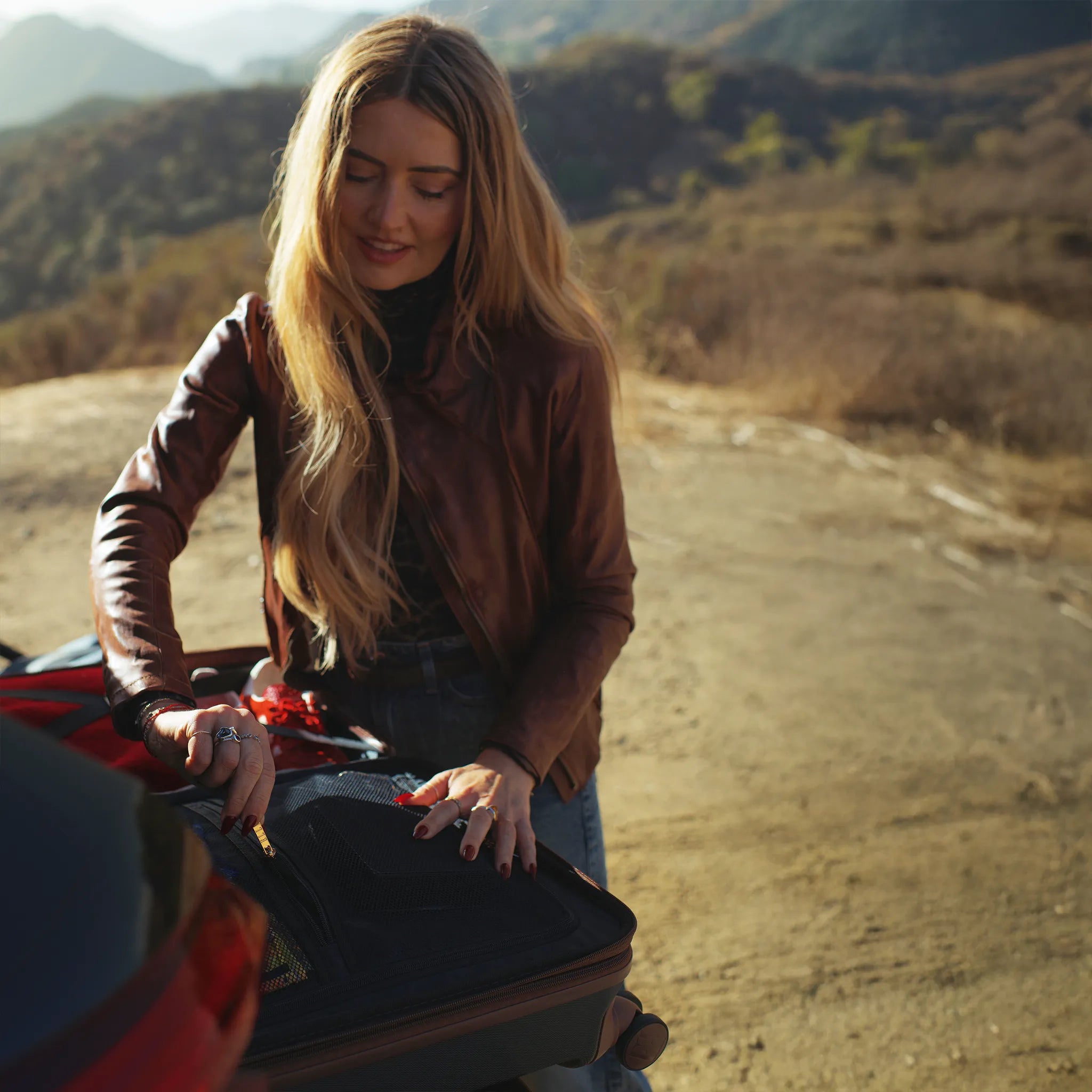 Woman standing next to a motorcycle on a dirt road with mountains in the background