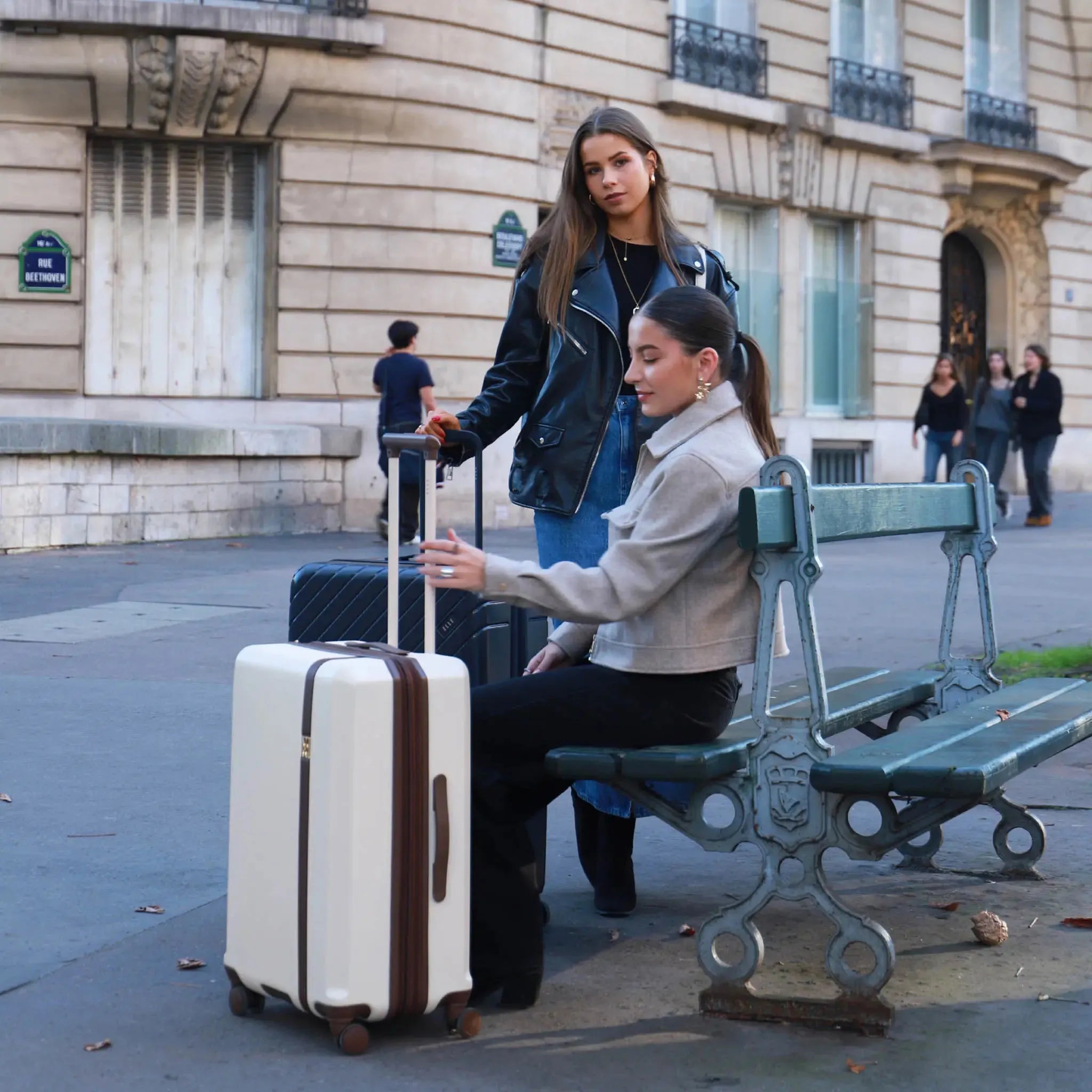 Two women with luggage on a street in an urban setting