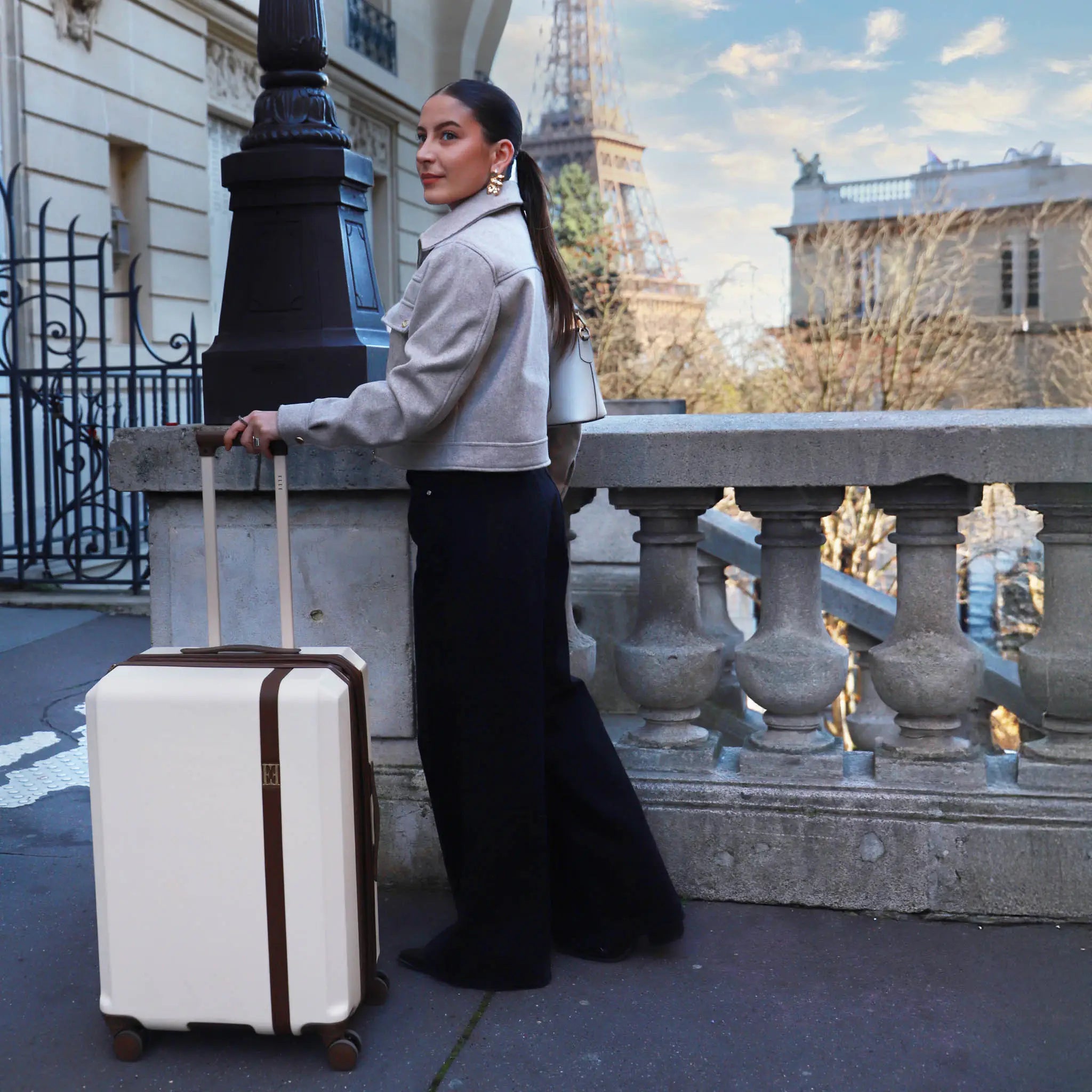Woman with a suitcase standing in front of a building with a view of the Eiffel Tower.