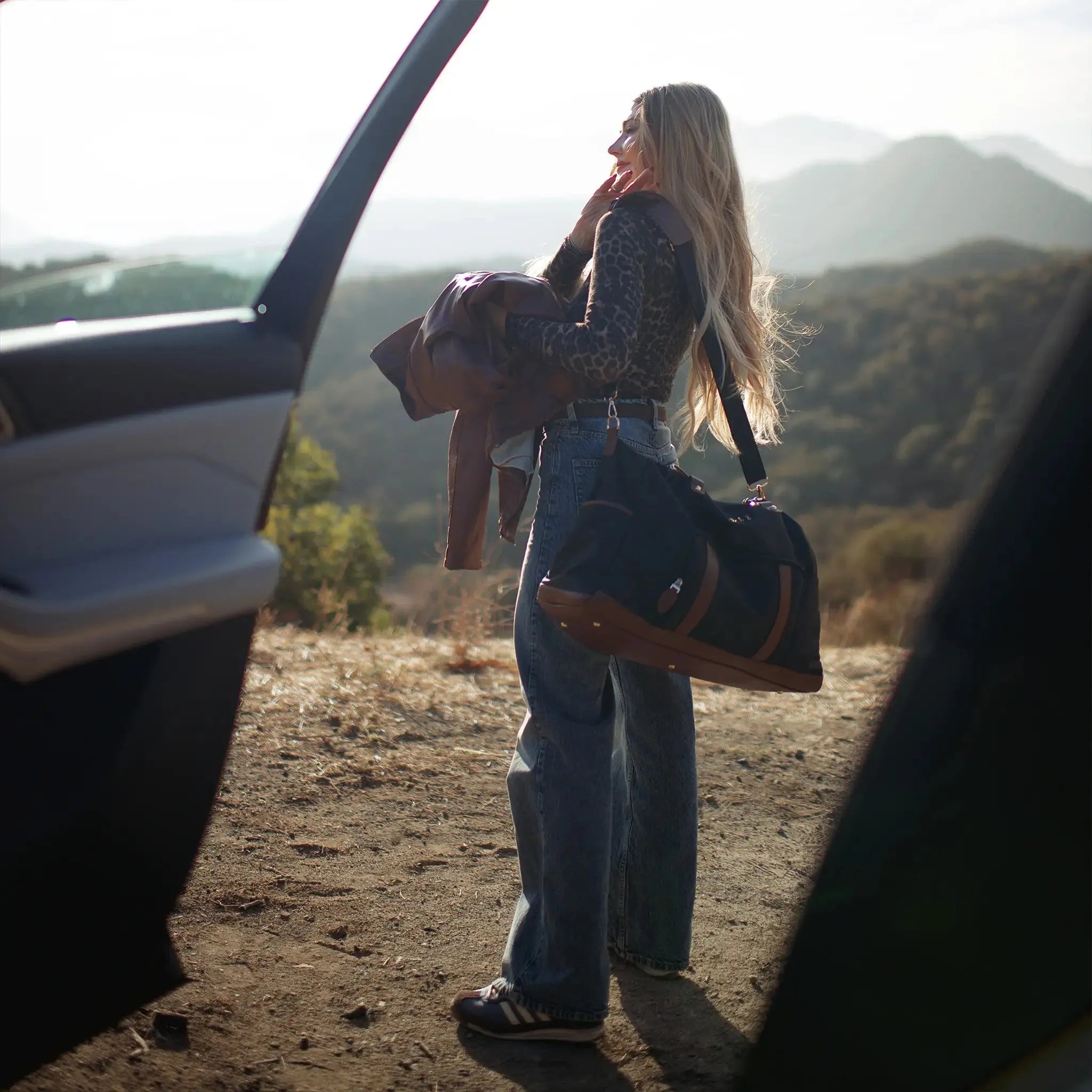 Woman standing by a car with mountains in the background