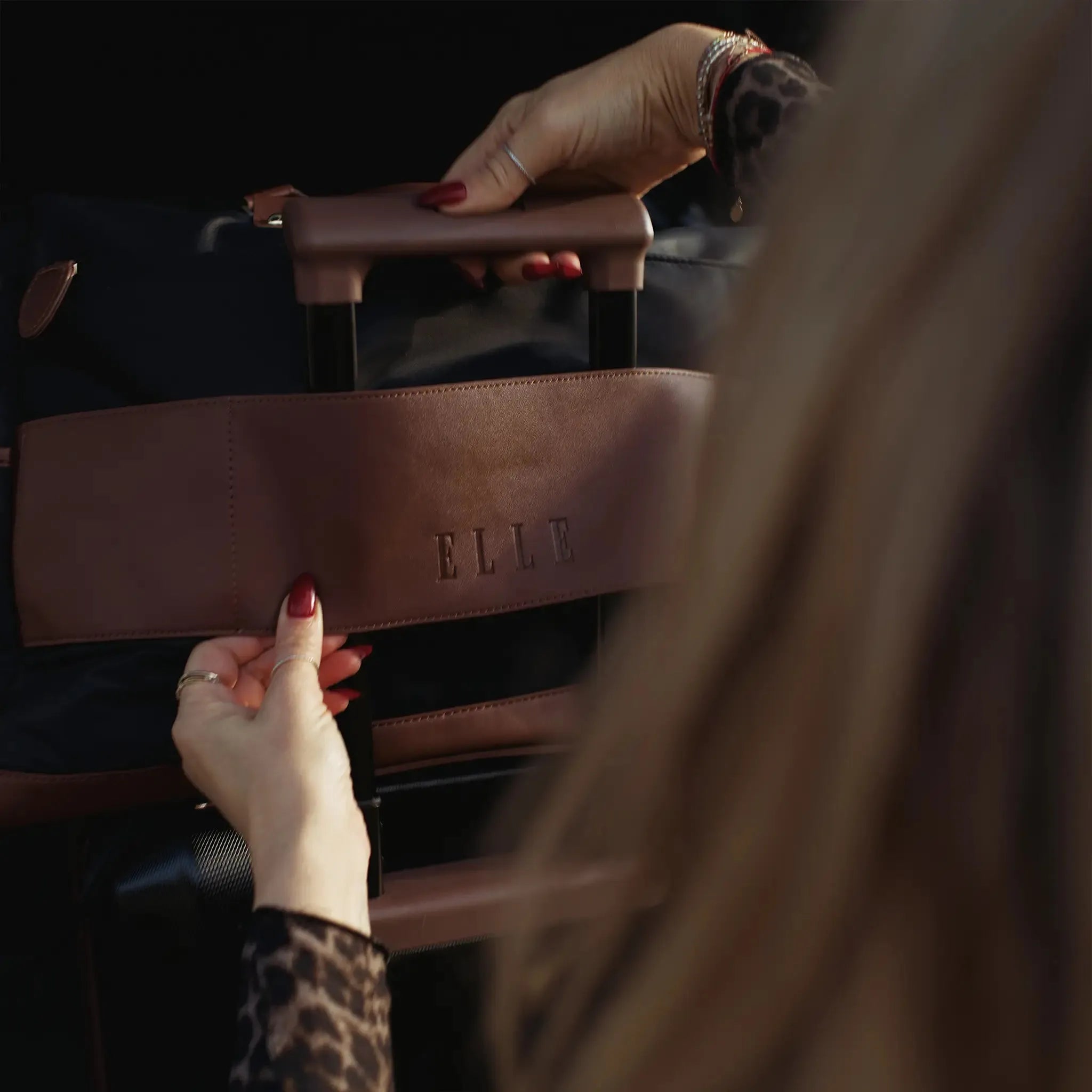 Person holding a brown handbag with 'ELLE' branding.