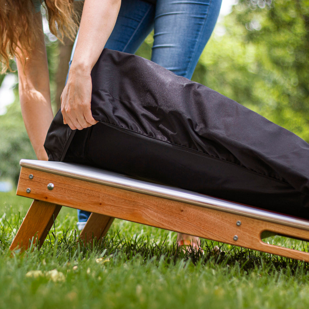 Person opening a black garment bag on a wooden bench outdoors.