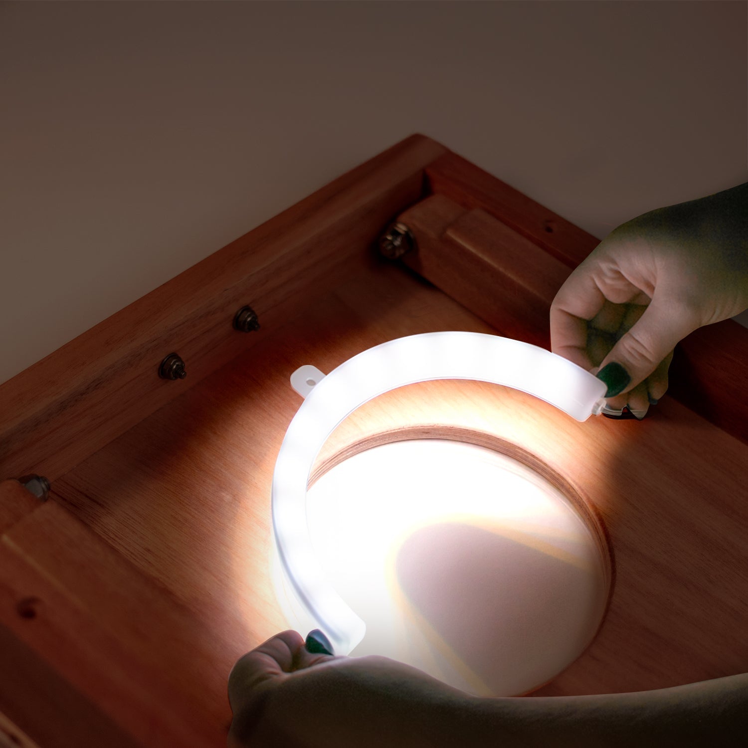 Person holding a round, white LED light on a wooden surface