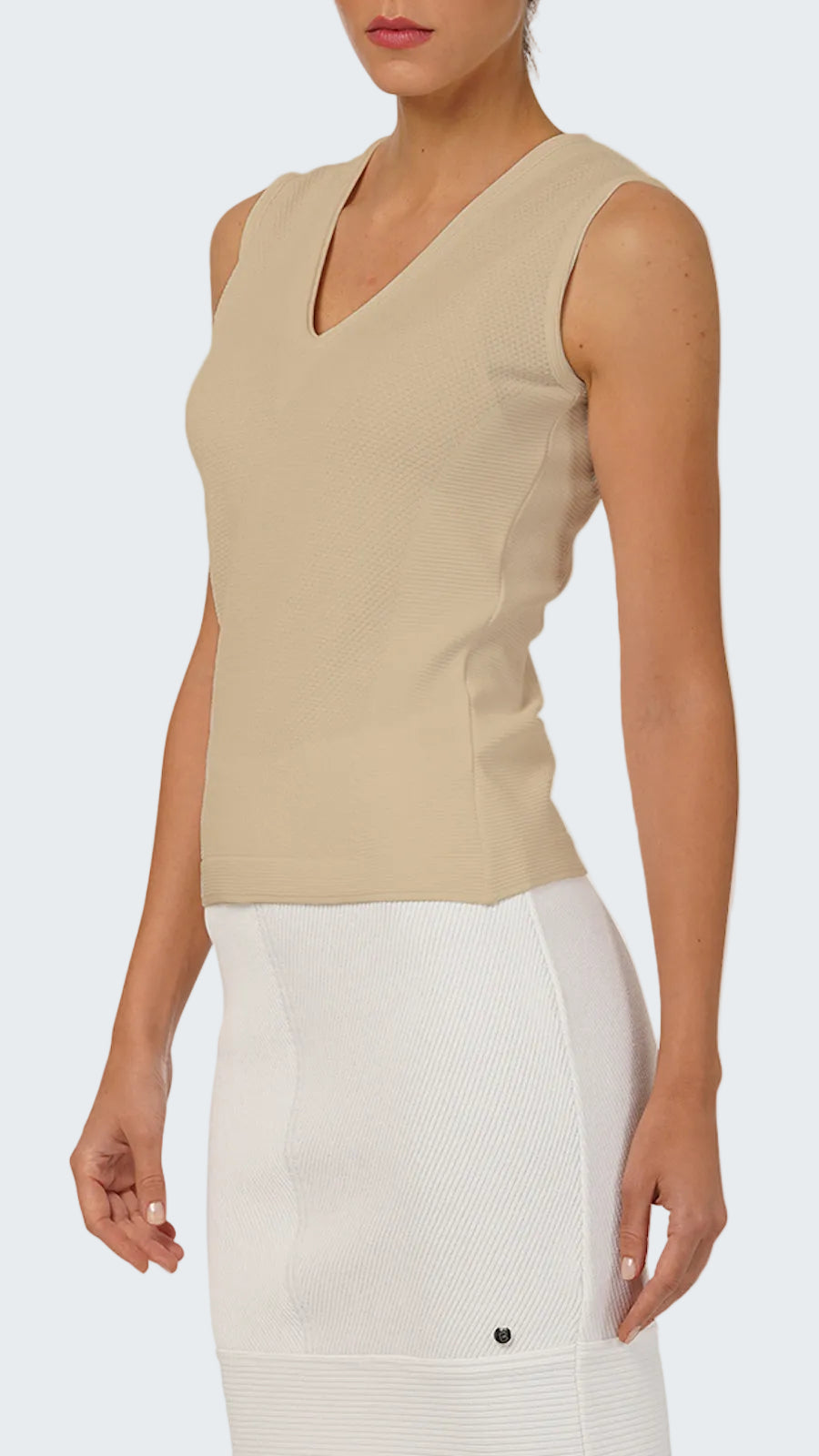 Woman wearing a beige sleeveless top and white pants on a white background
