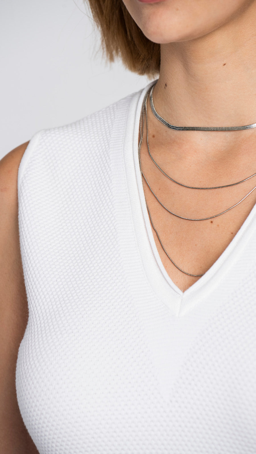 Close-up of a person wearing multiple necklaces on a white background
