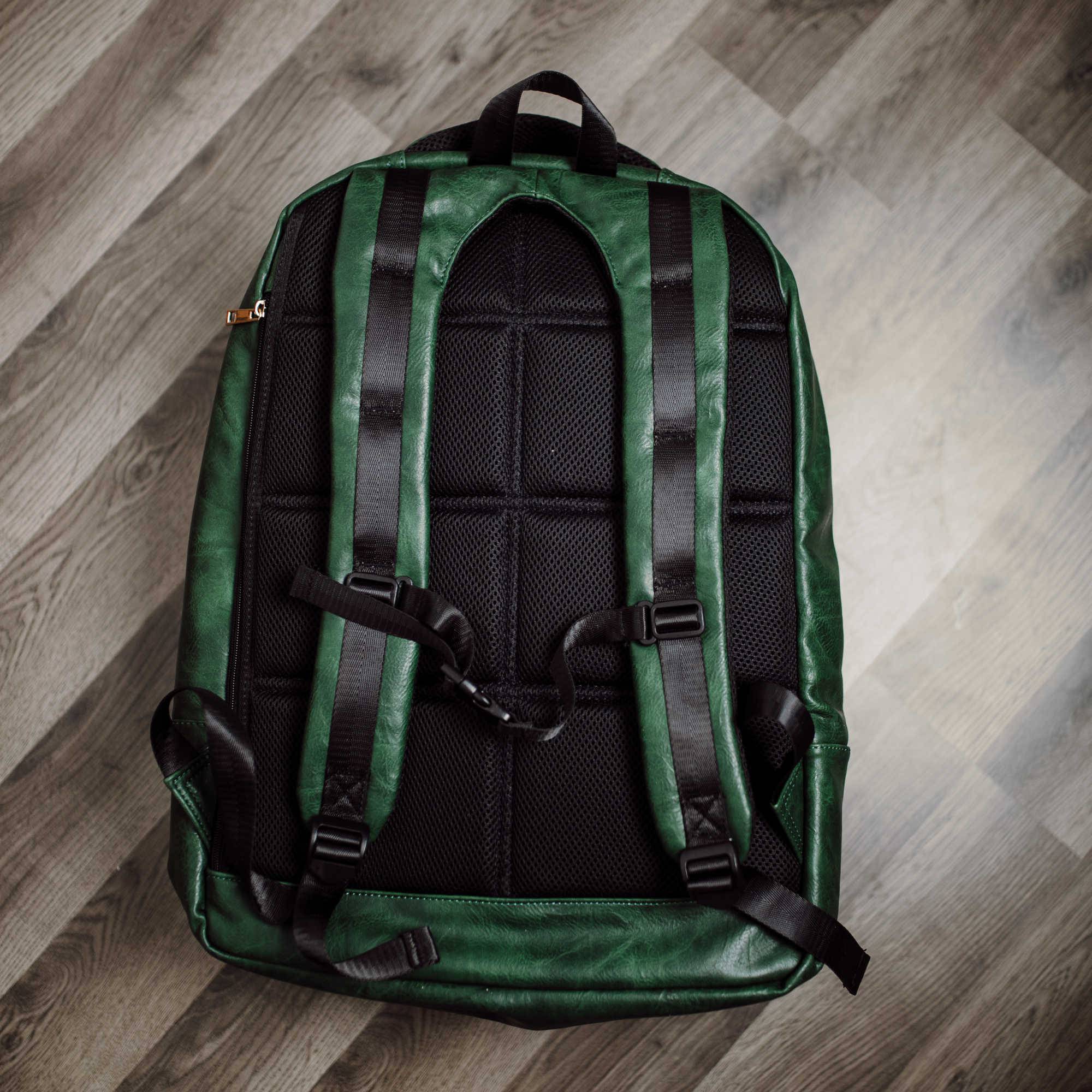 Green backpack with black straps on a wooden floor