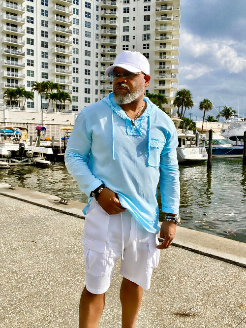 Man in light blue shirt and white shorts standing by a waterfront with buildings in the background