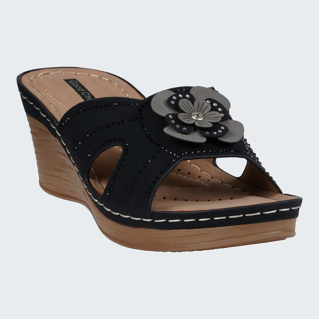 Black wedge sandal with a flower detail on a white background