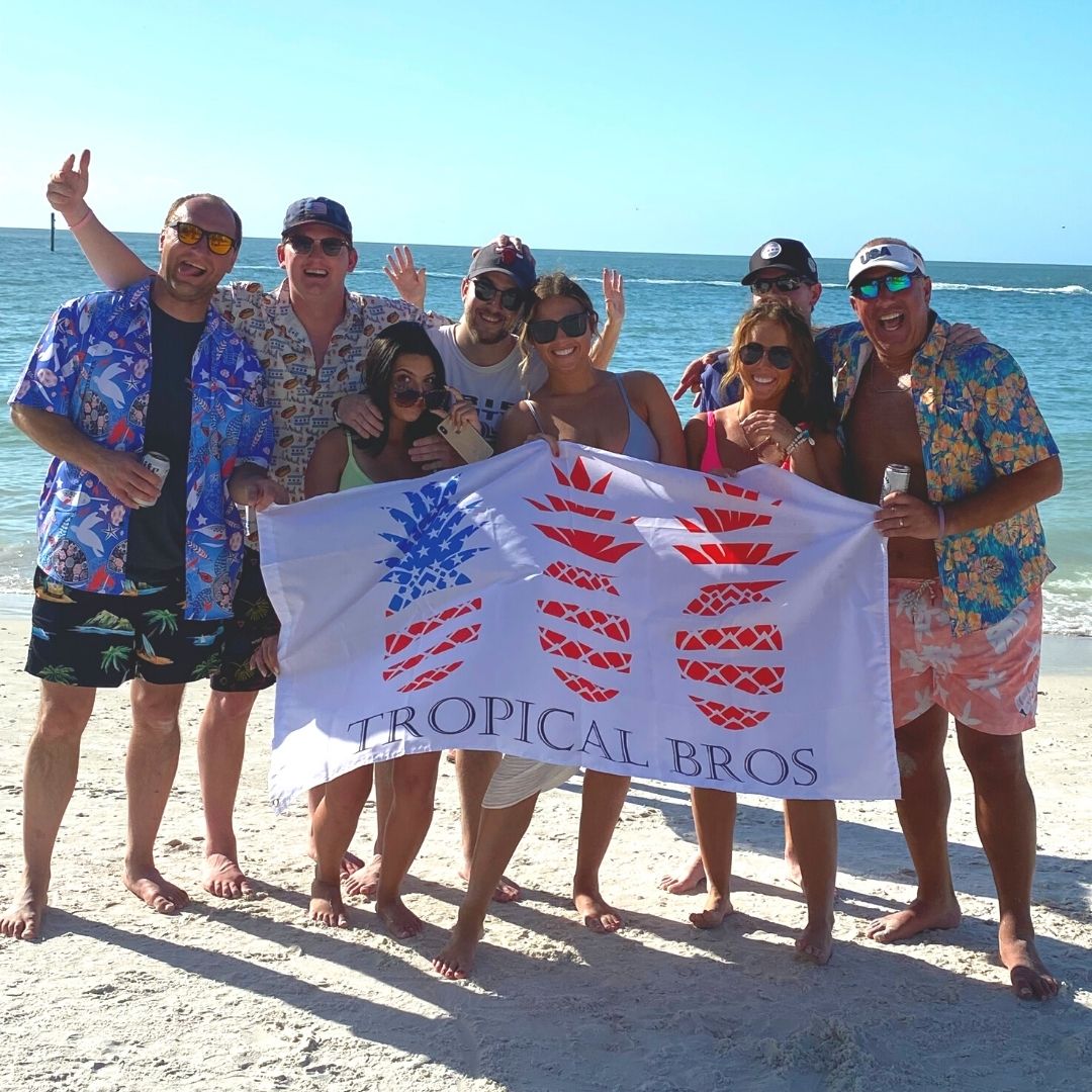 Group of people on a beach holding a 'Tropical Bros' banner