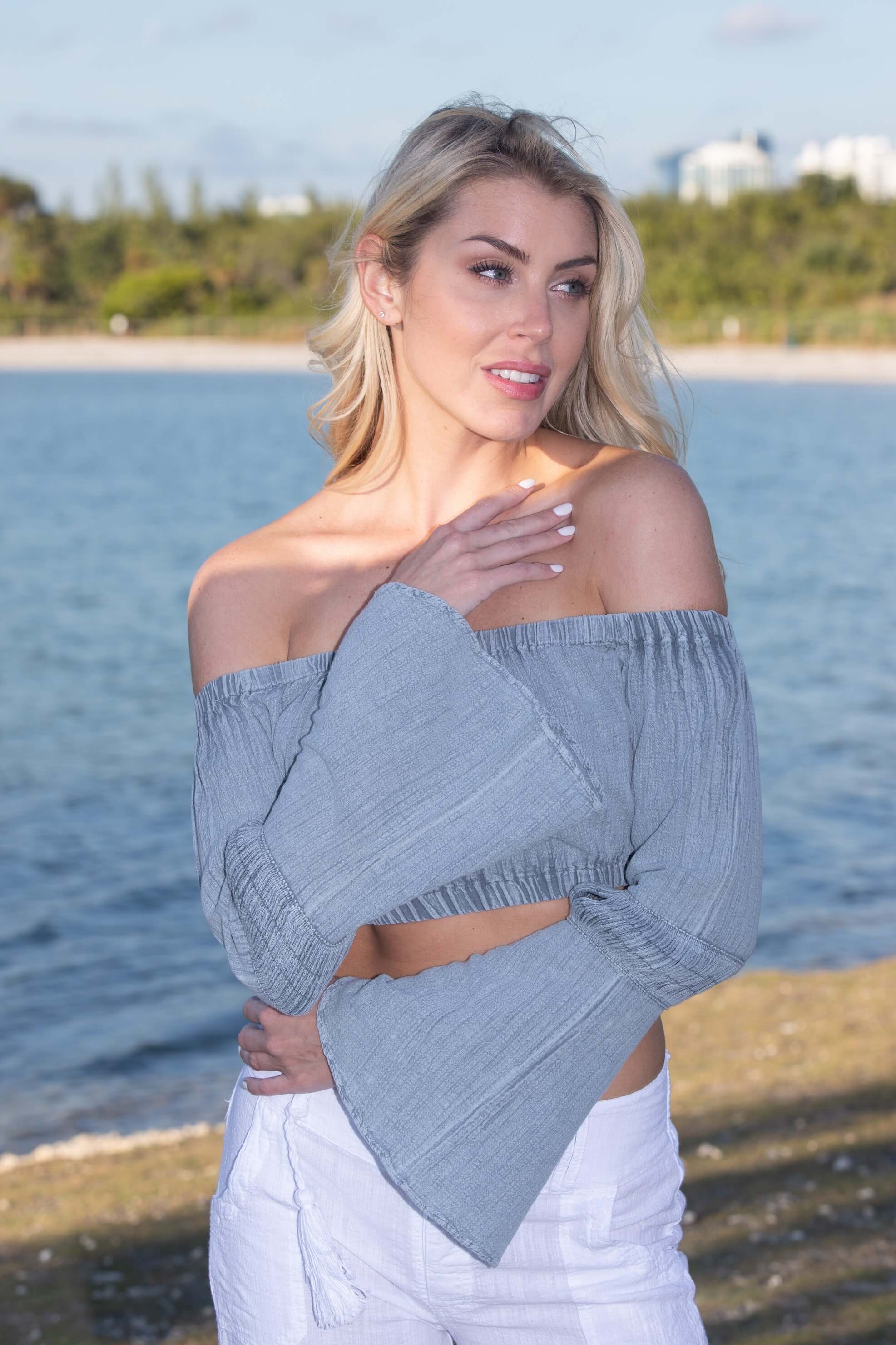 Woman wearing a gray off-shoulder top by a body of water
