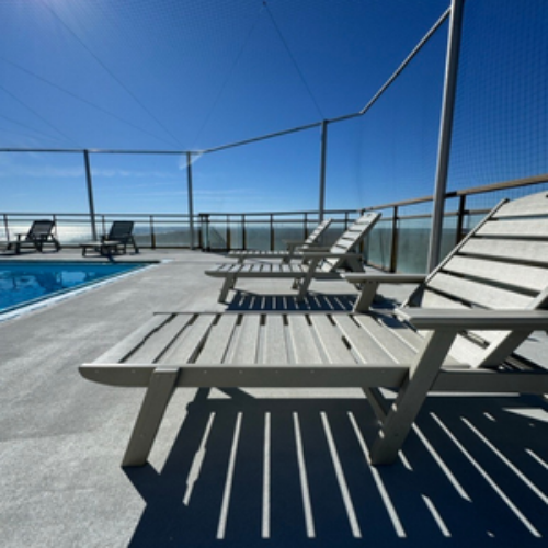 Beach chairs on a deck with a pool and ocean view under a clear blue sky.