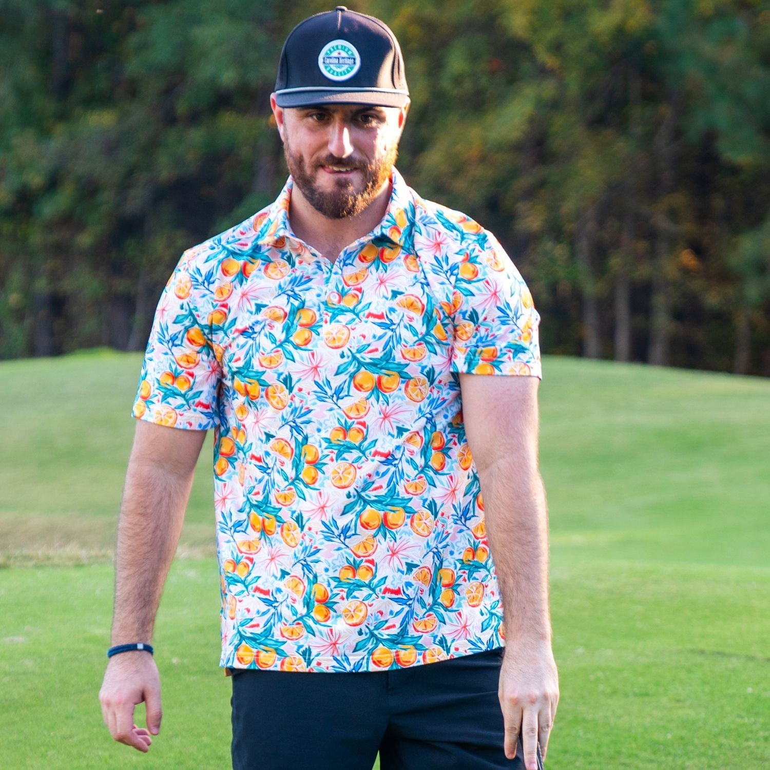 Man wearing a colorful floral shirt and dark cap on a grassy field