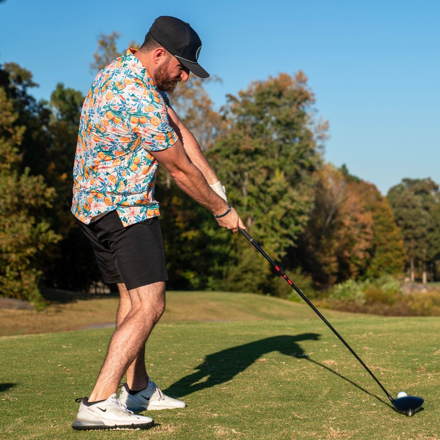 Man playing golf on a sunny day with trees in the background