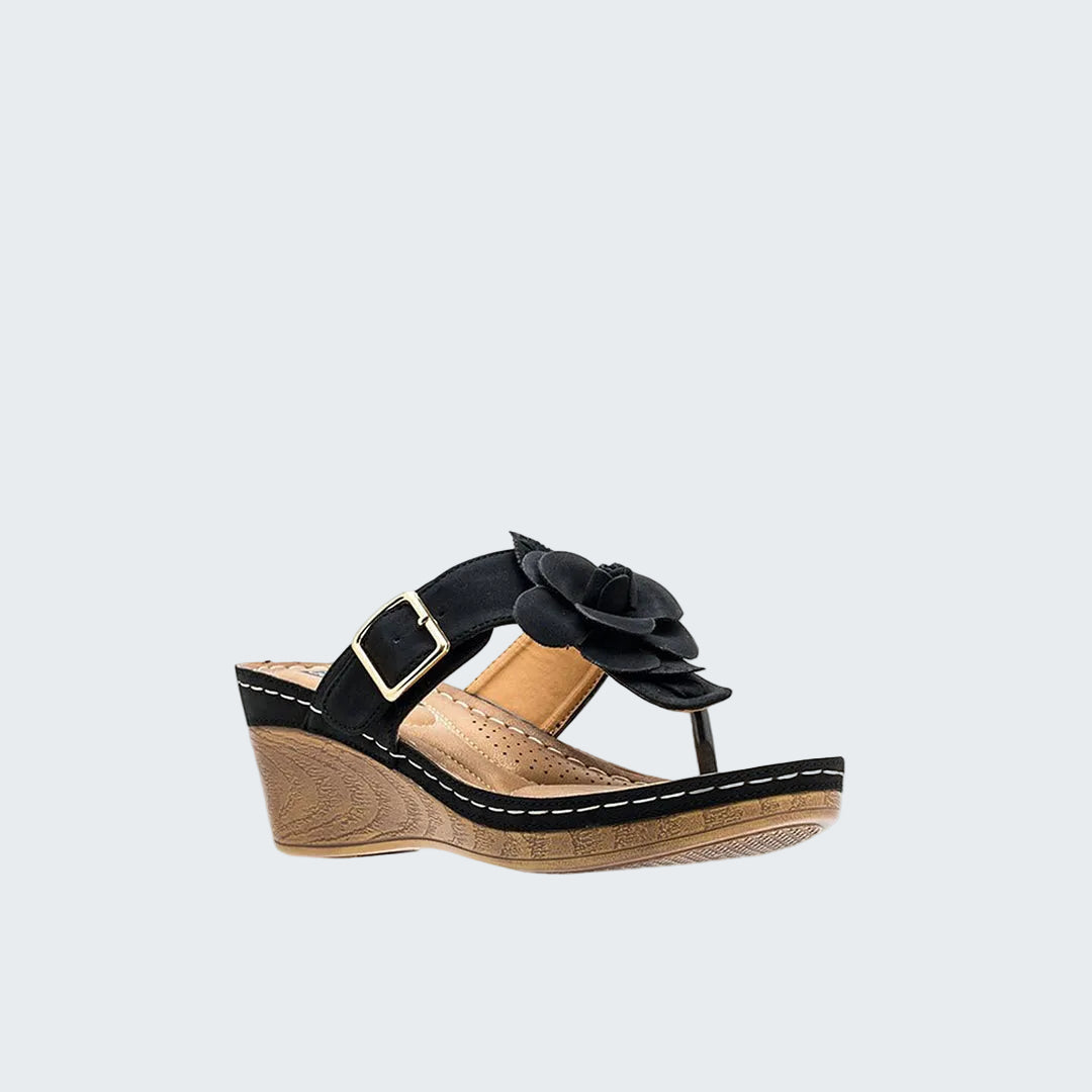 Black wedge sandal with a flower detail on a white background