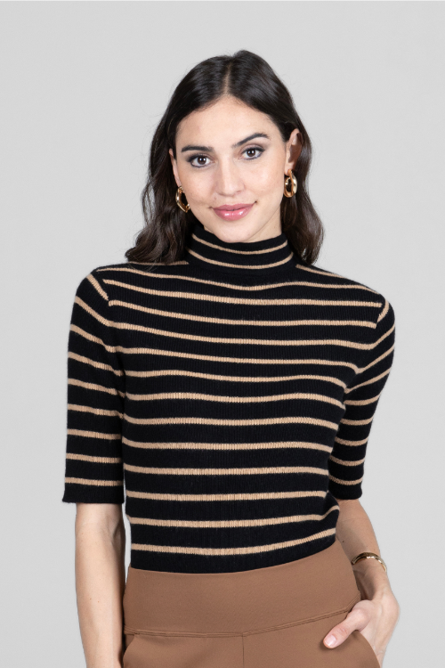Woman wearing a black and beige striped turtleneck sweater against a gray background