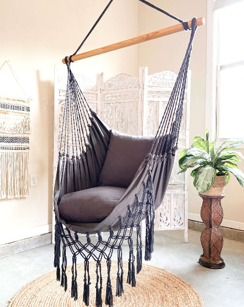 Gray hammock chair with wooden rod in a room with a plant and decorative elements.
