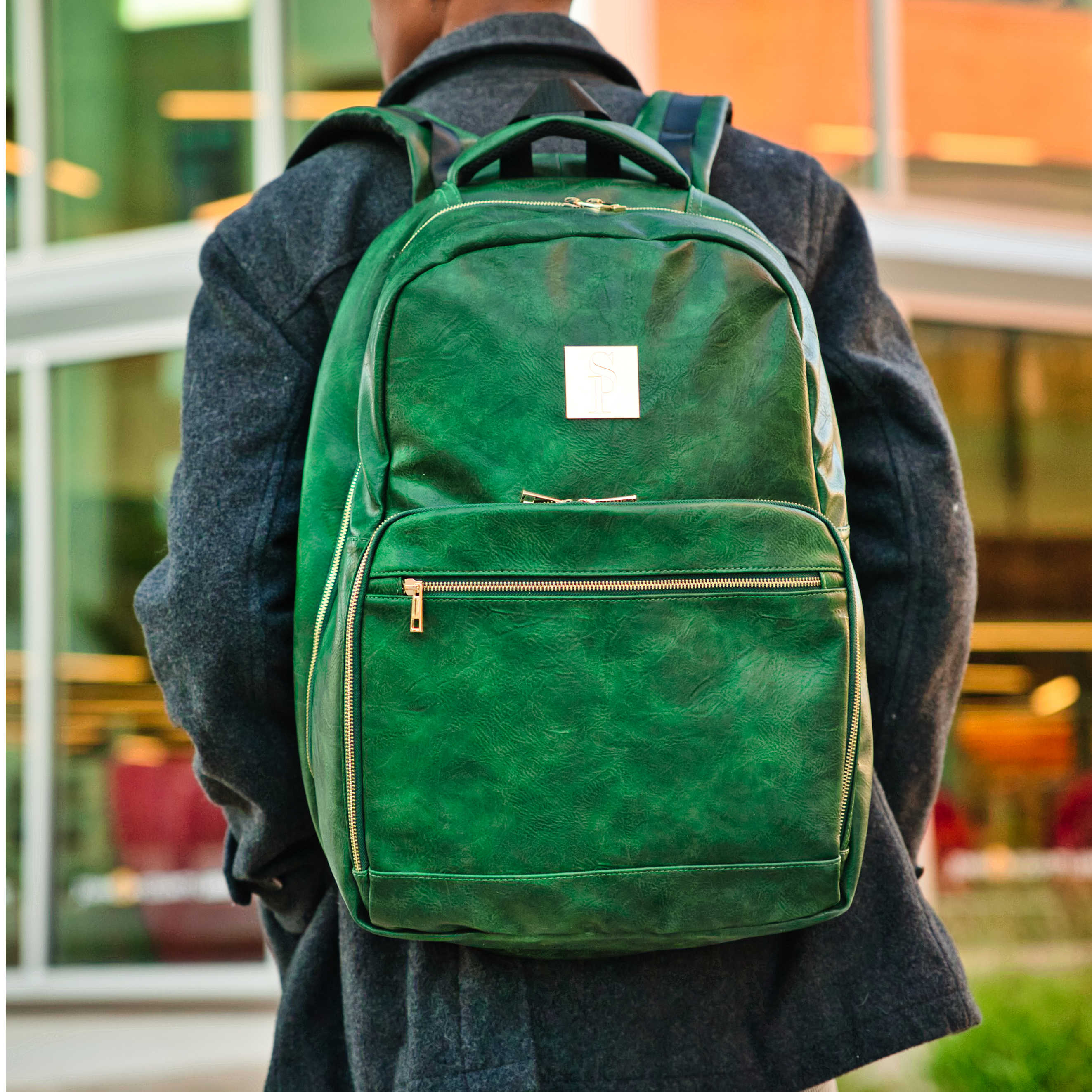 Person wearing a green backpack with a blurred indoor background