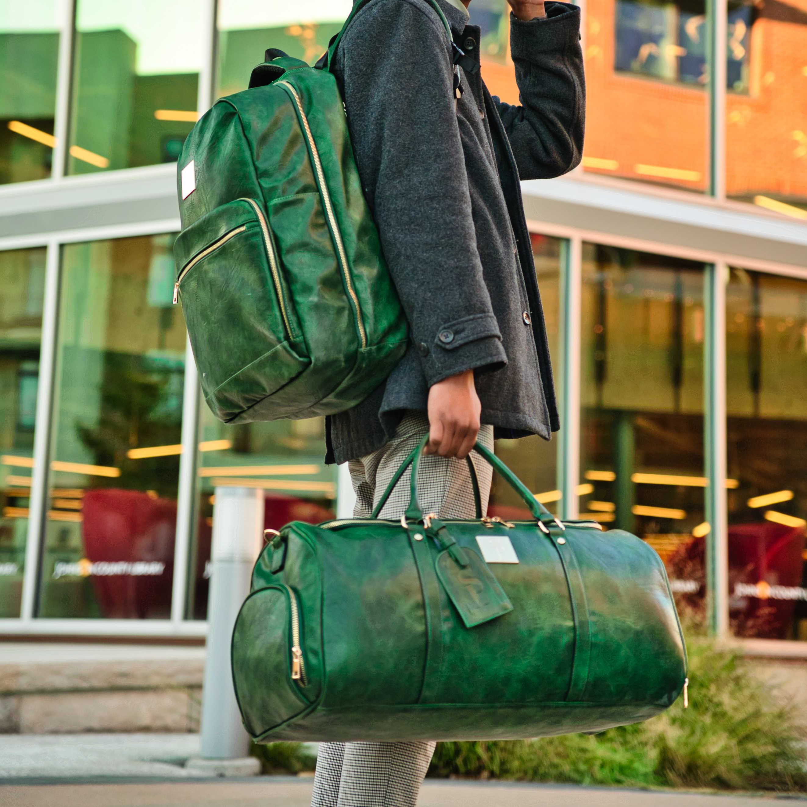 Person holding a green backpack and duffel bag in front of a building.