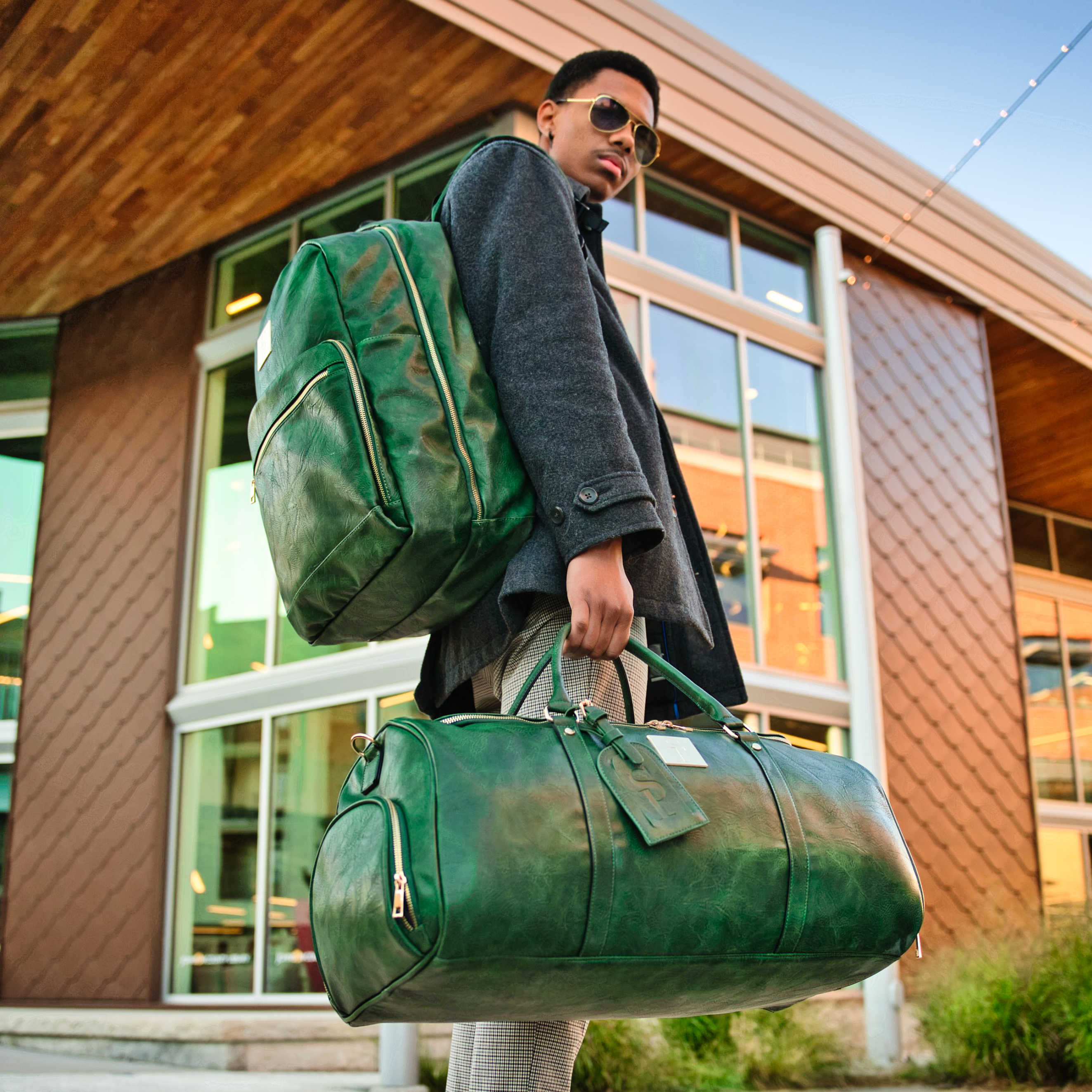 Man holding a green leather duffel bag in front of a building