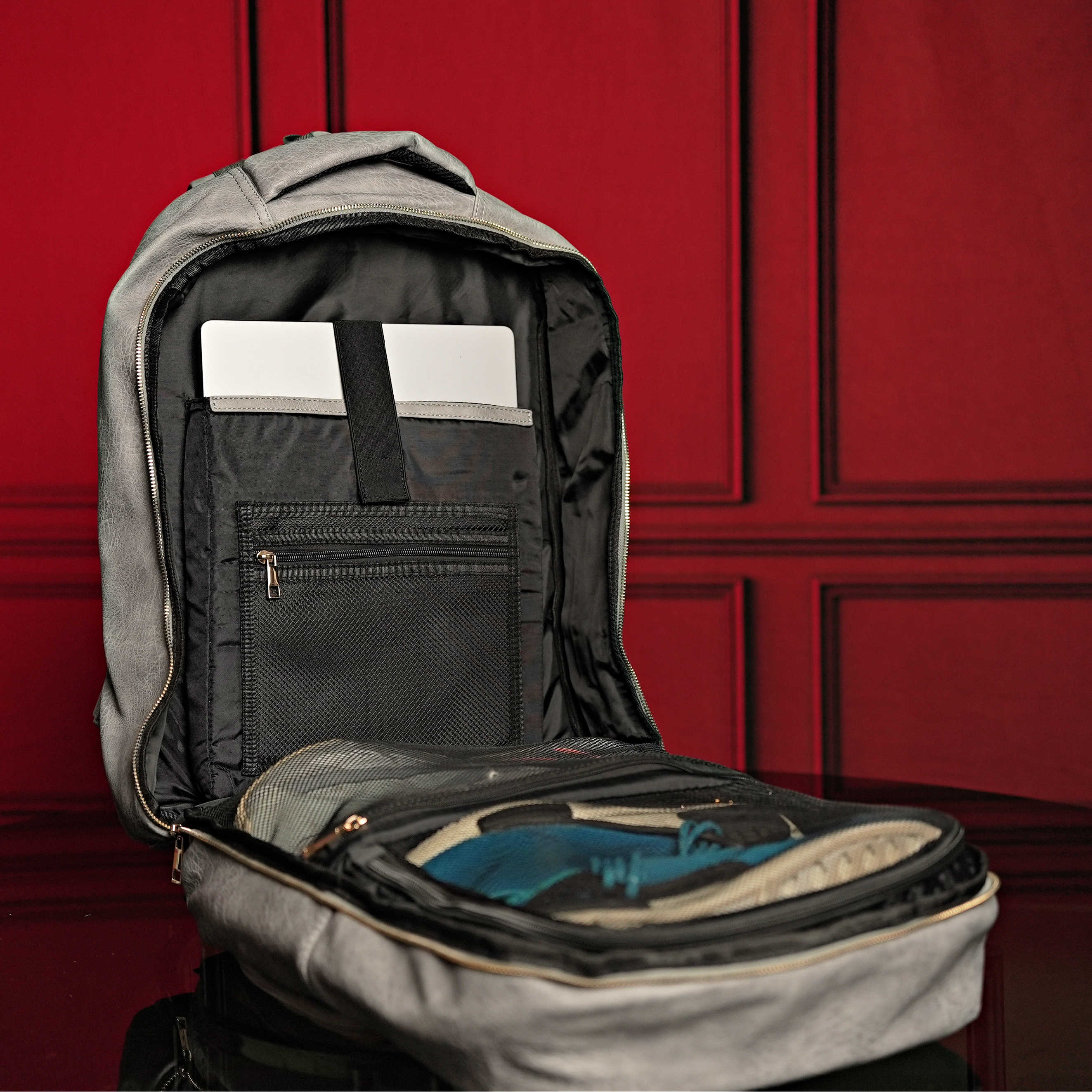 Gray backpack with open compartments against a red paneled wall