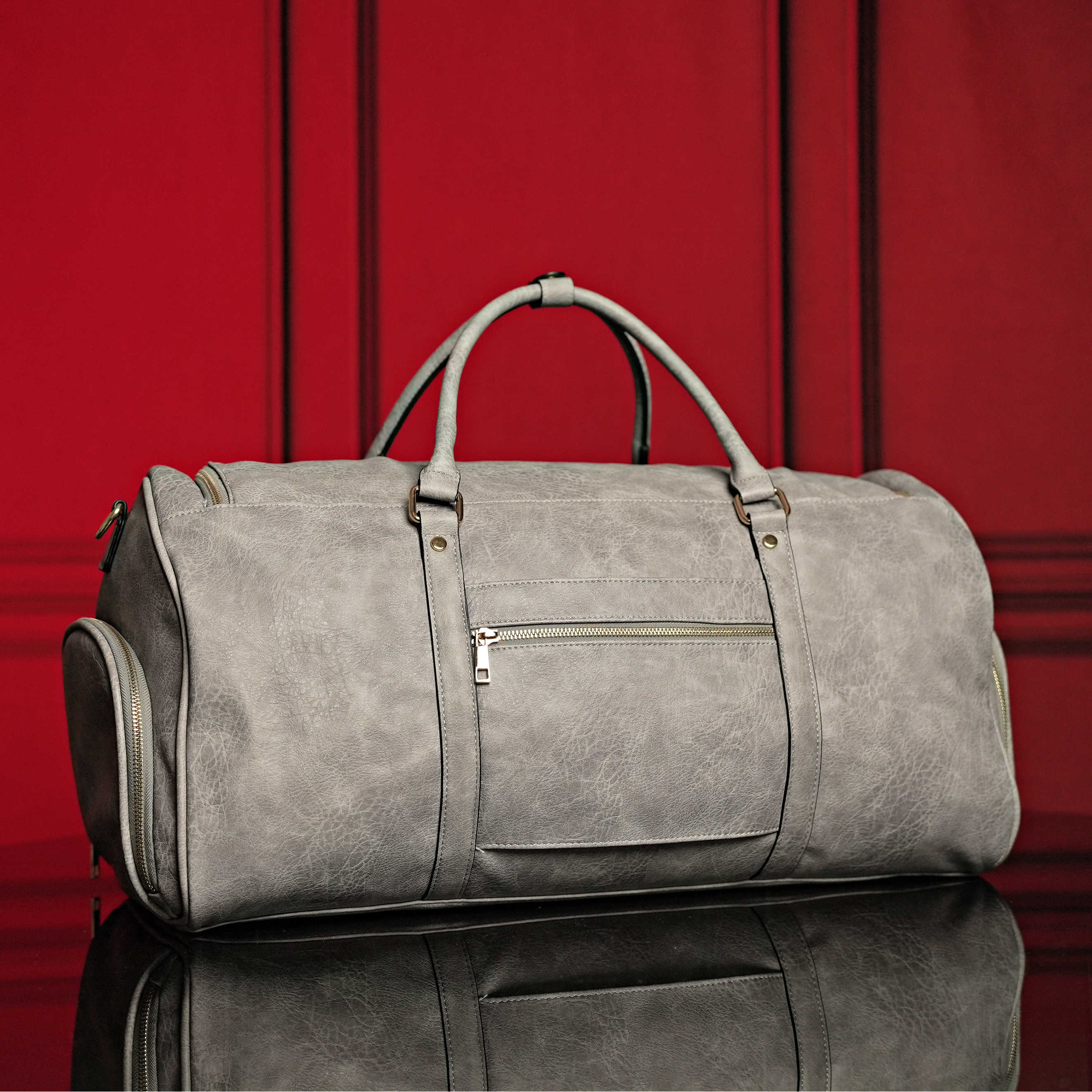 Gray duffel bag on a reflective surface with a red curtain background