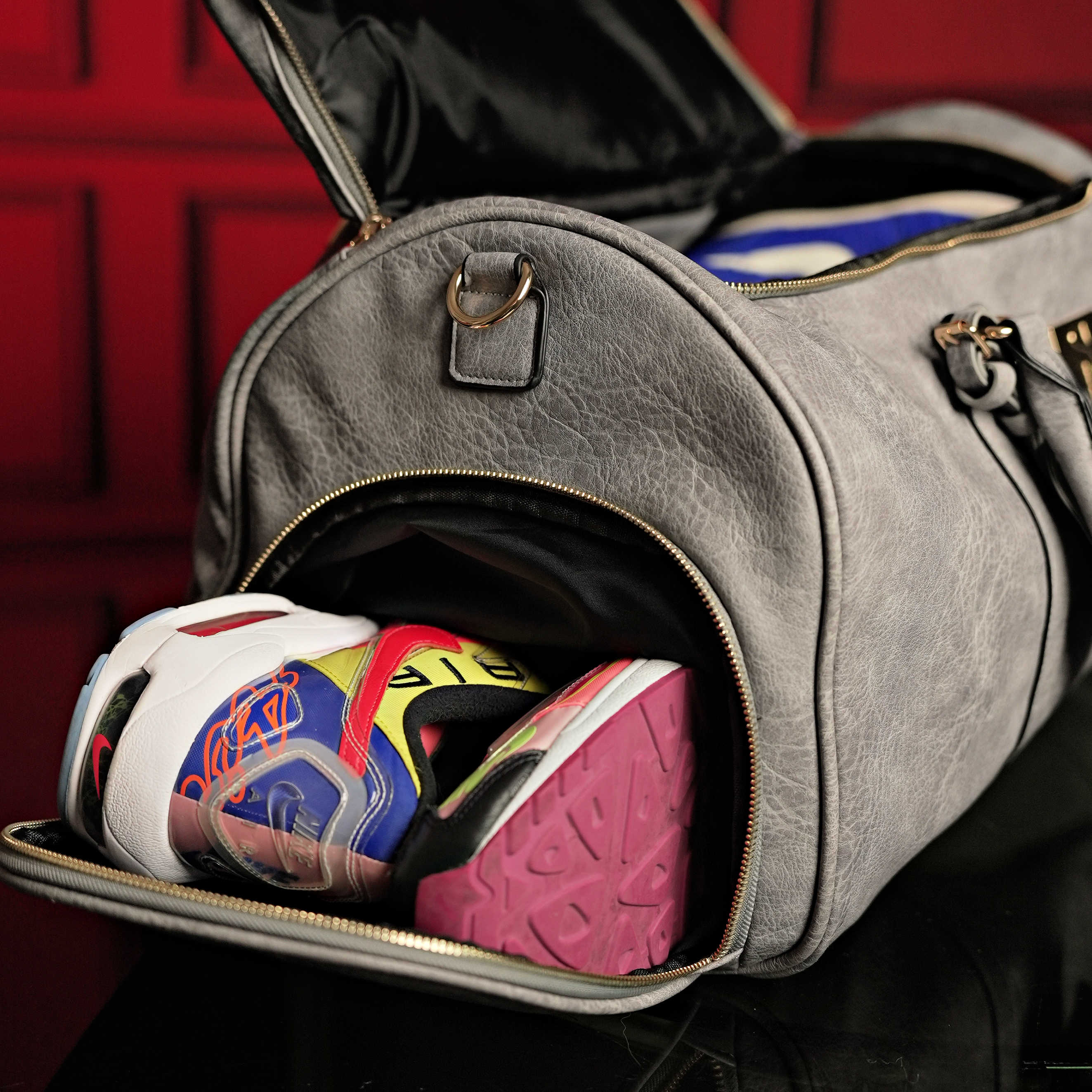 Gray duffel bag with colorful shoes inside against a red background