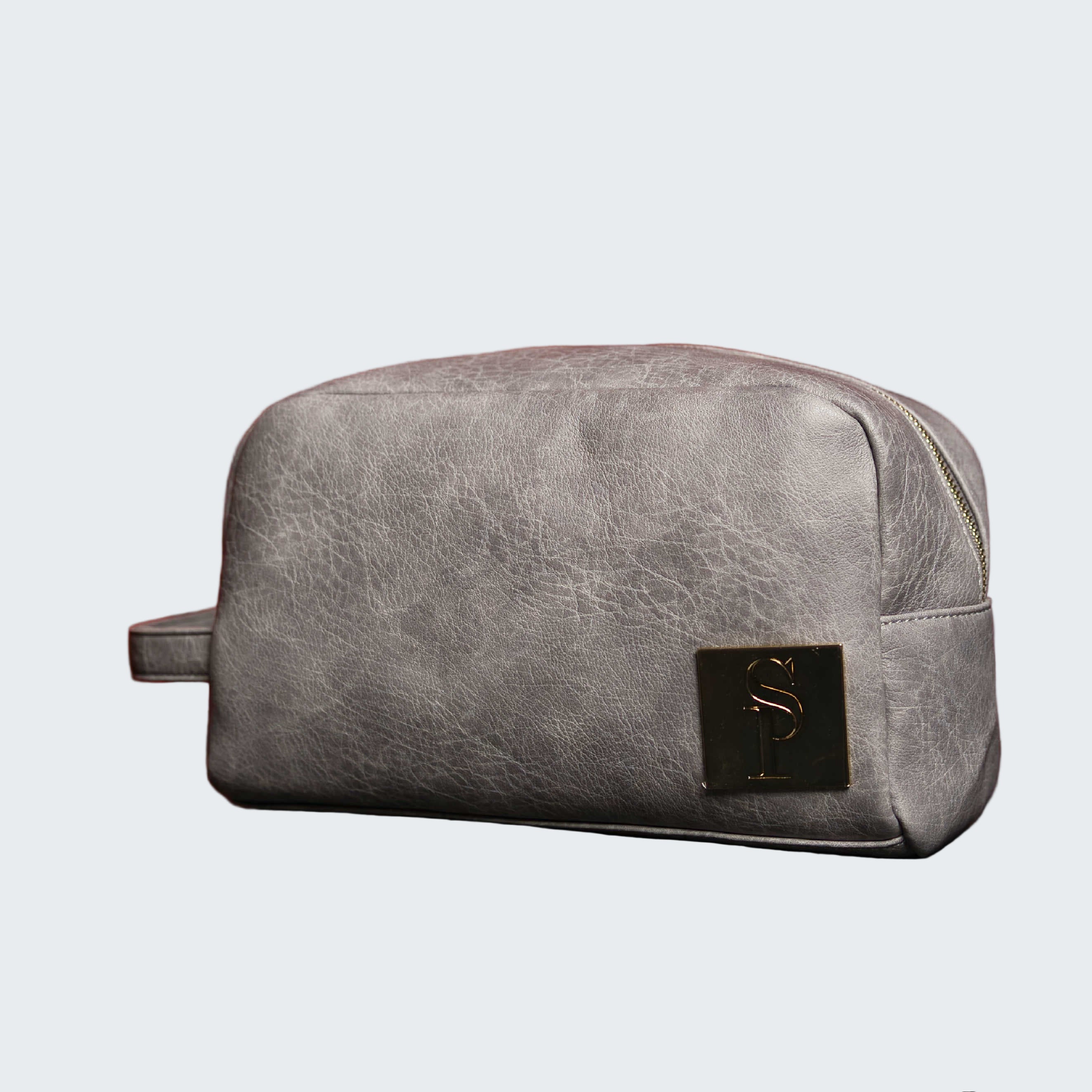 Gray leather toiletry bag with a brand logo on a reflective surface and red background
