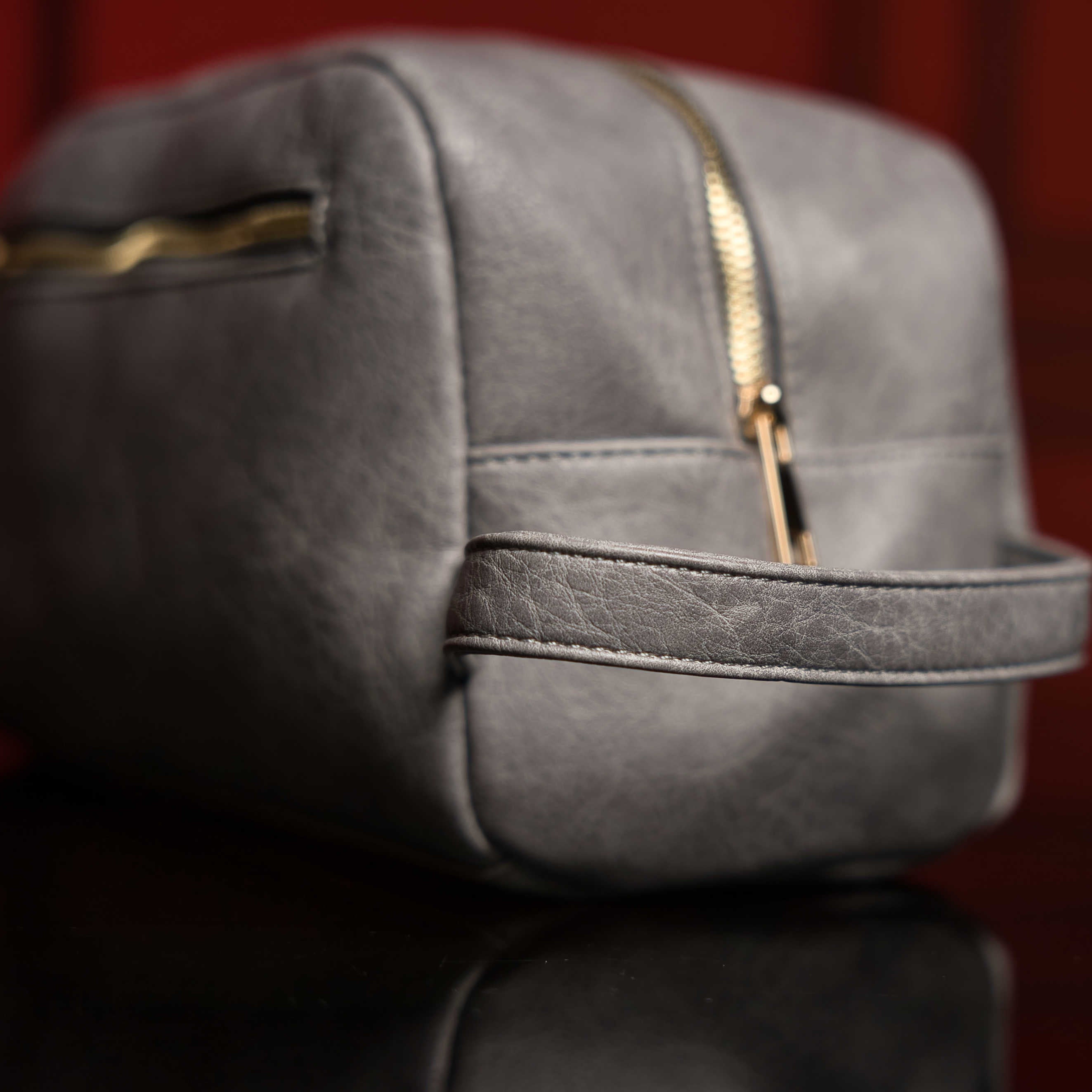 Gray leather bag with gold zipper on a reflective surface with a blurred red background
