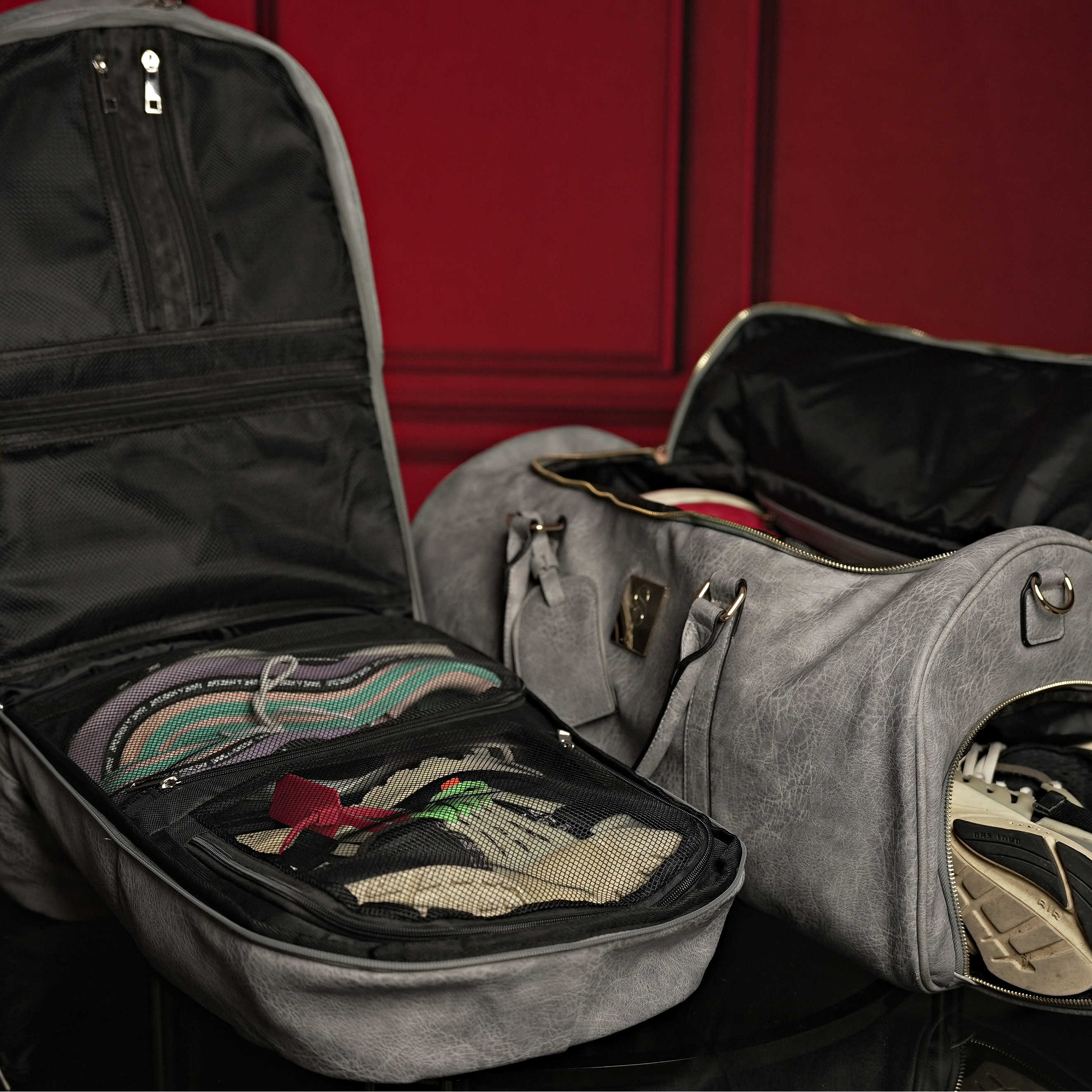 Two open bags, one black and one gray, with clothes inside against a red background.