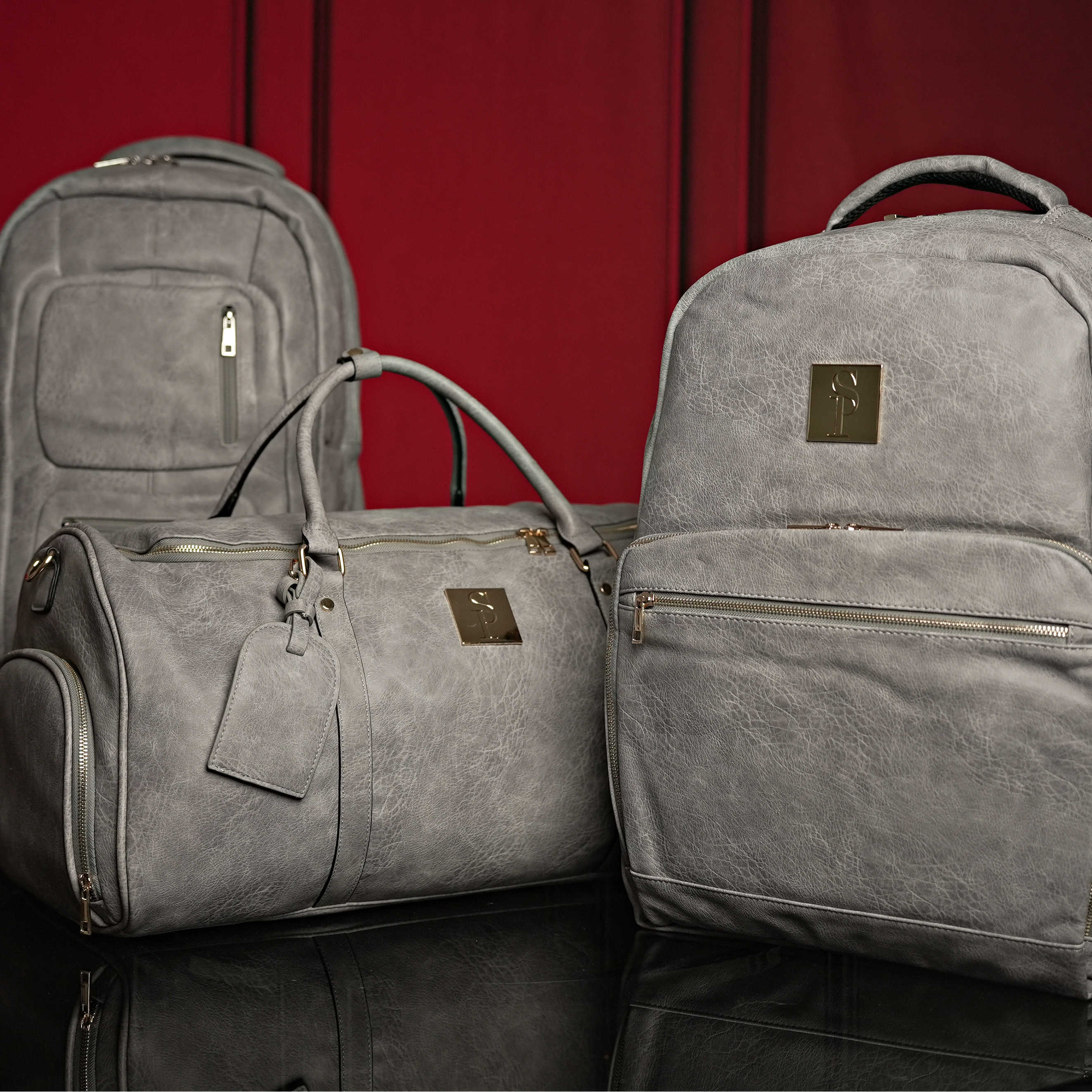 Gray bags including a backpack and duffel bag on a red background