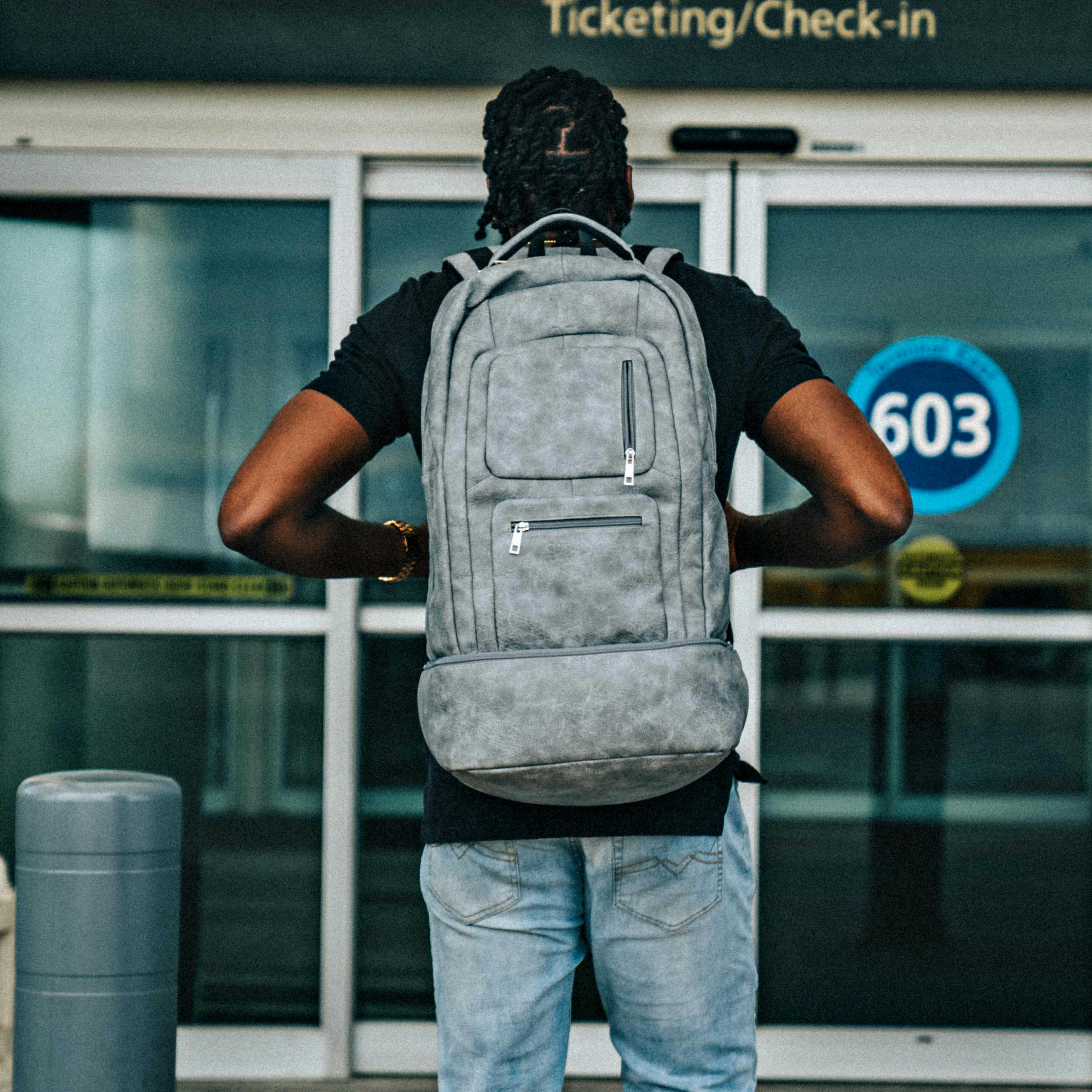 Person wearing a gray backpack in front of a building with '603' on the door.