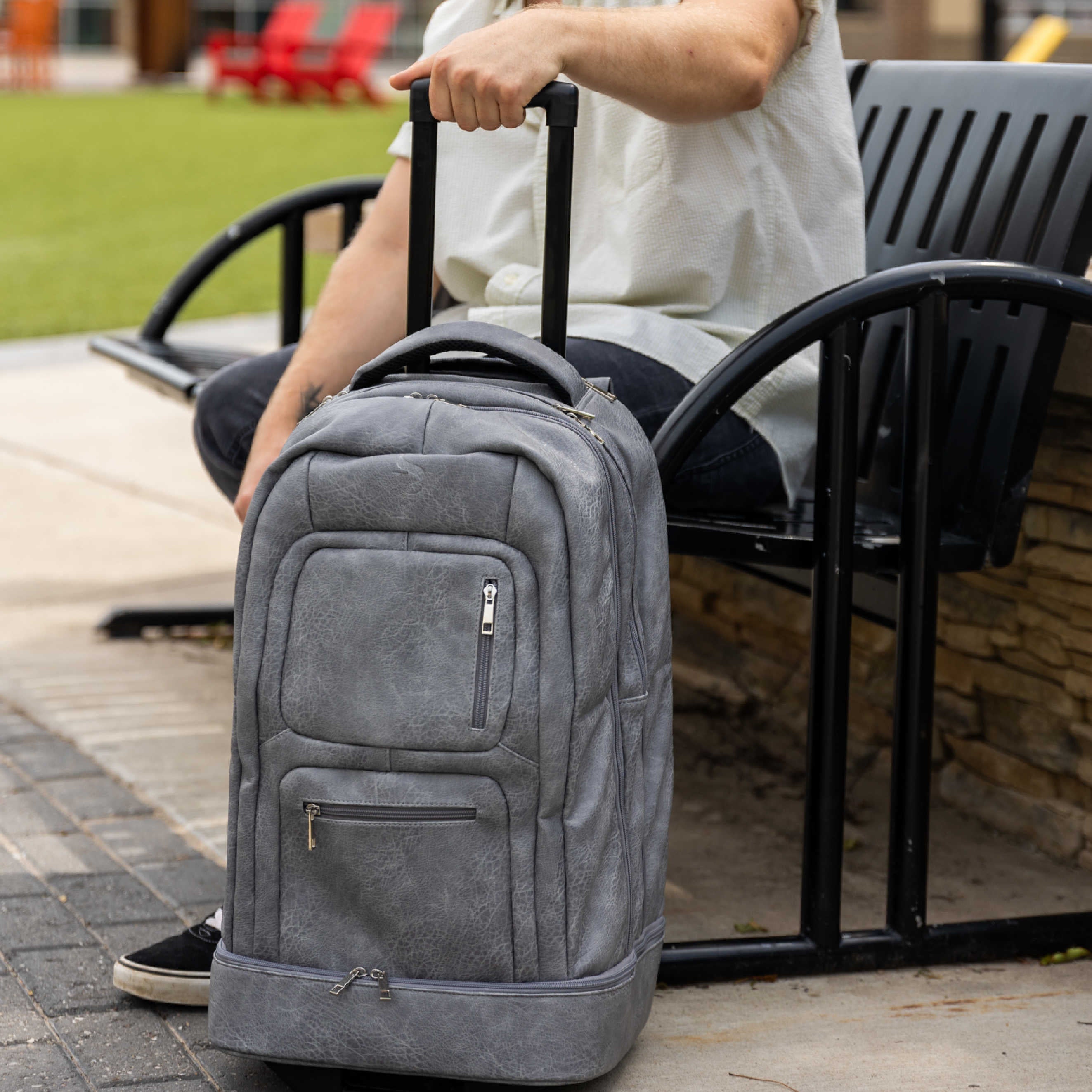 Person sitting on a bench with a gray backpack on a sidewalk