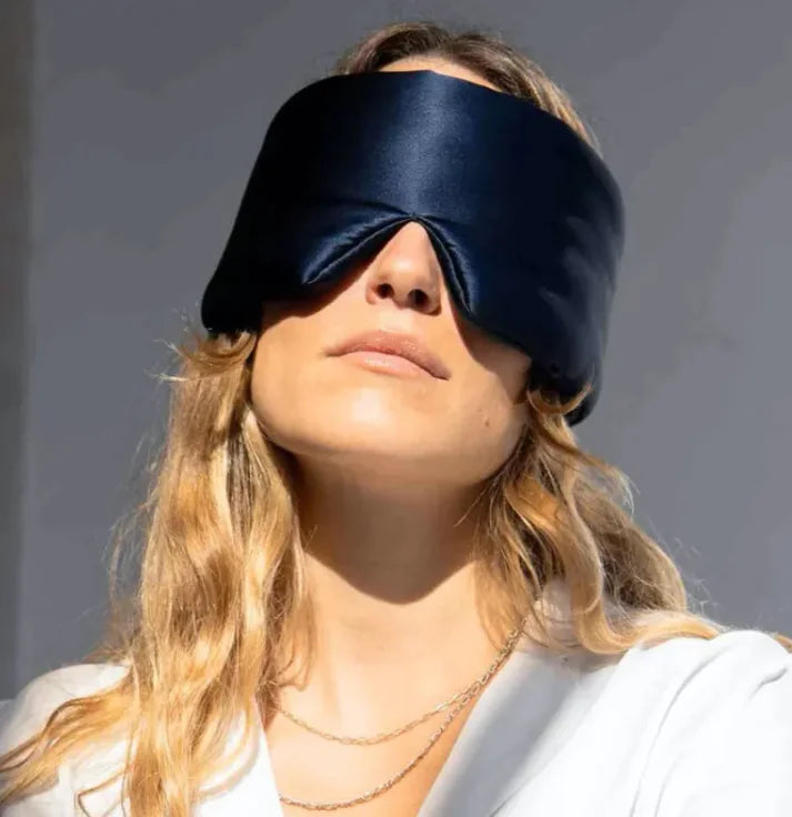 Person wearing a black sleep mask against a neutral background