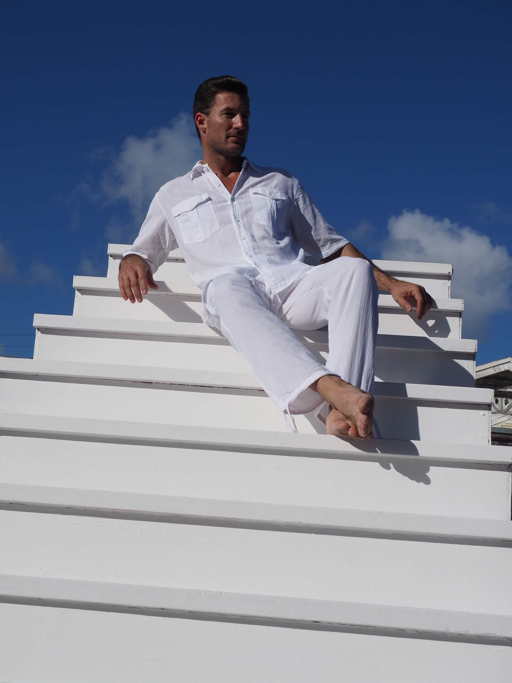 Man in white outfit sitting on a white staircase with a blue sky background