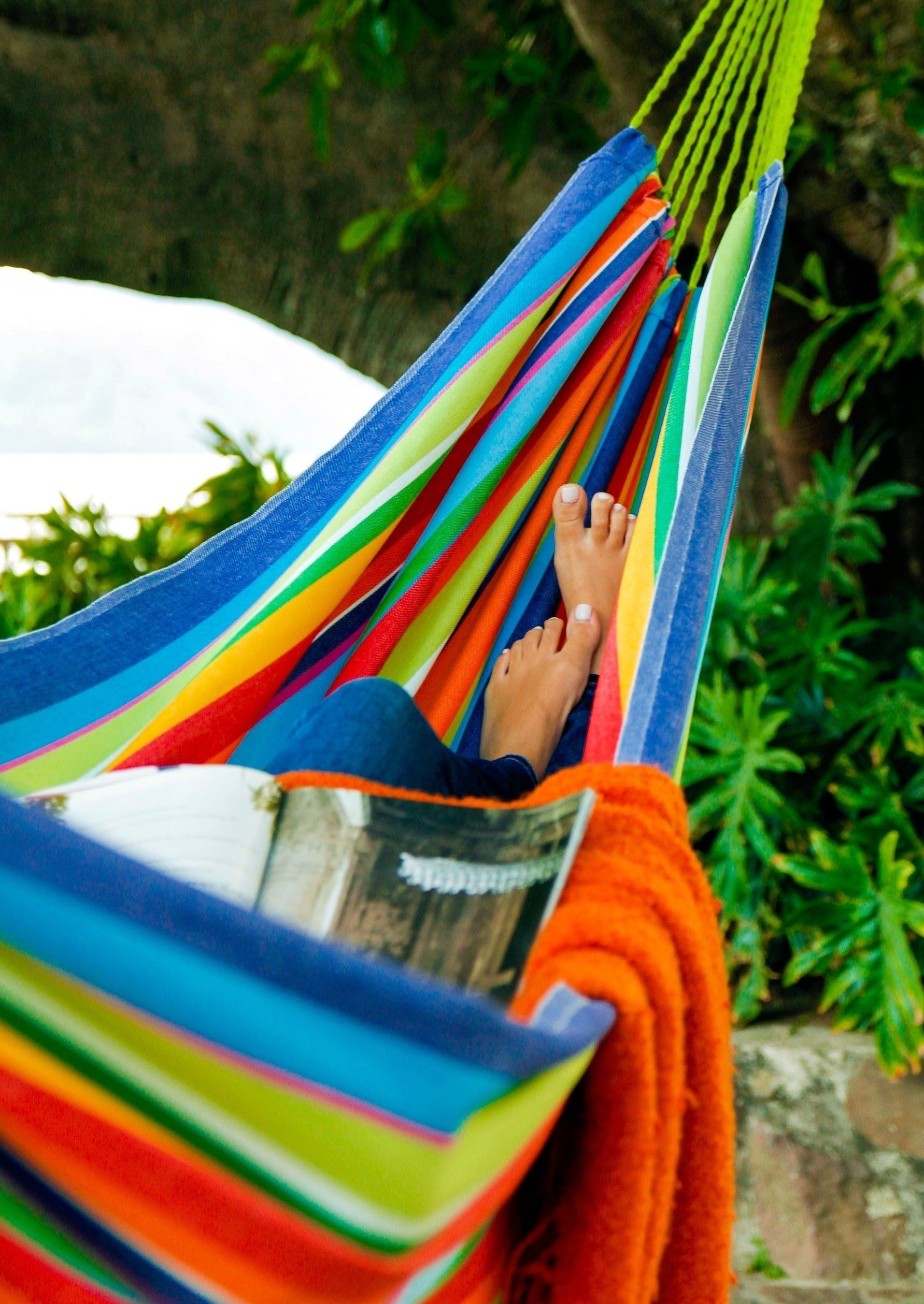 Colorful striped hammock with a person's feet inside, surrounded by greenery.