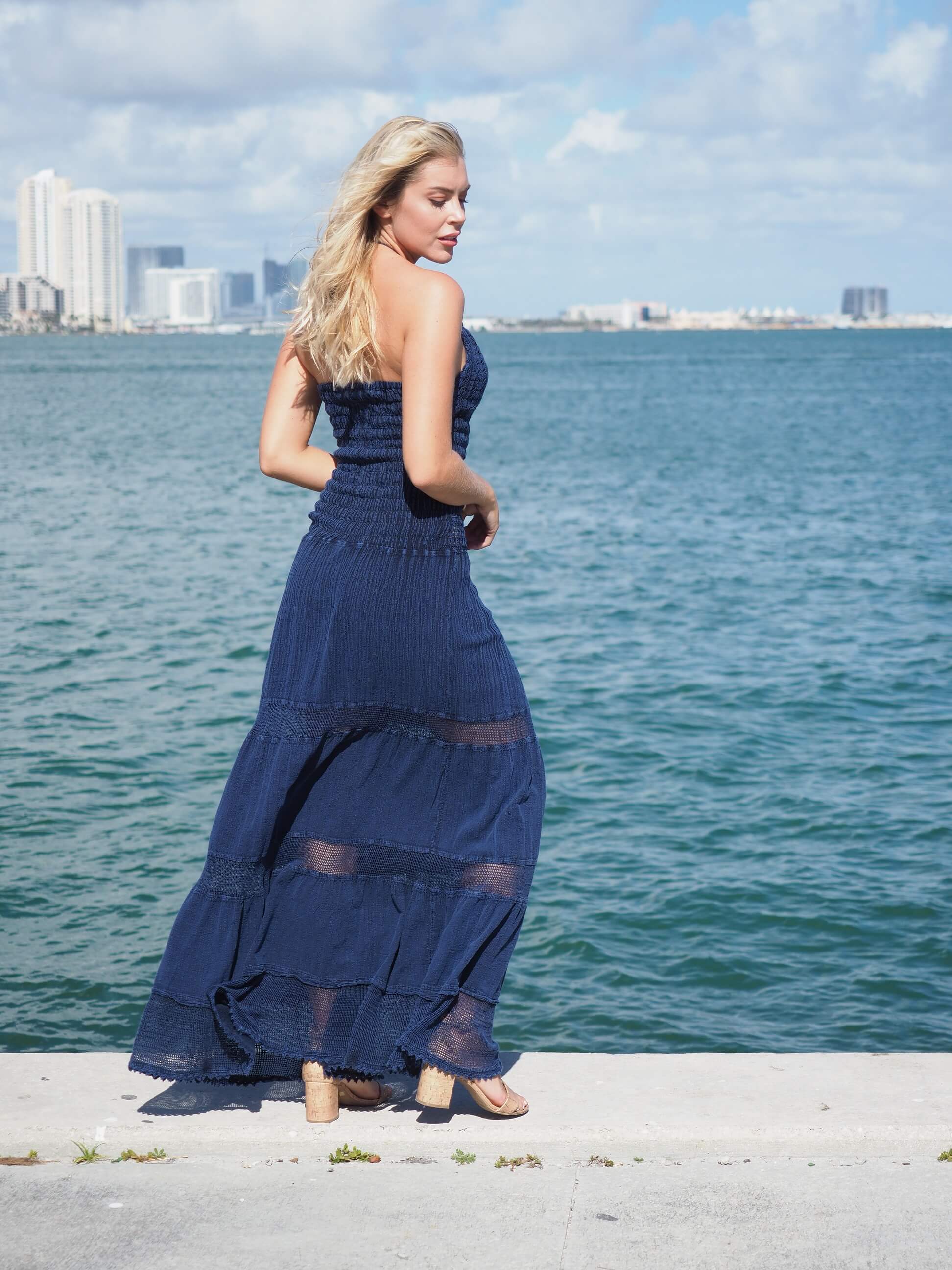 Woman in a blue dress standing by the water with a city skyline in the background