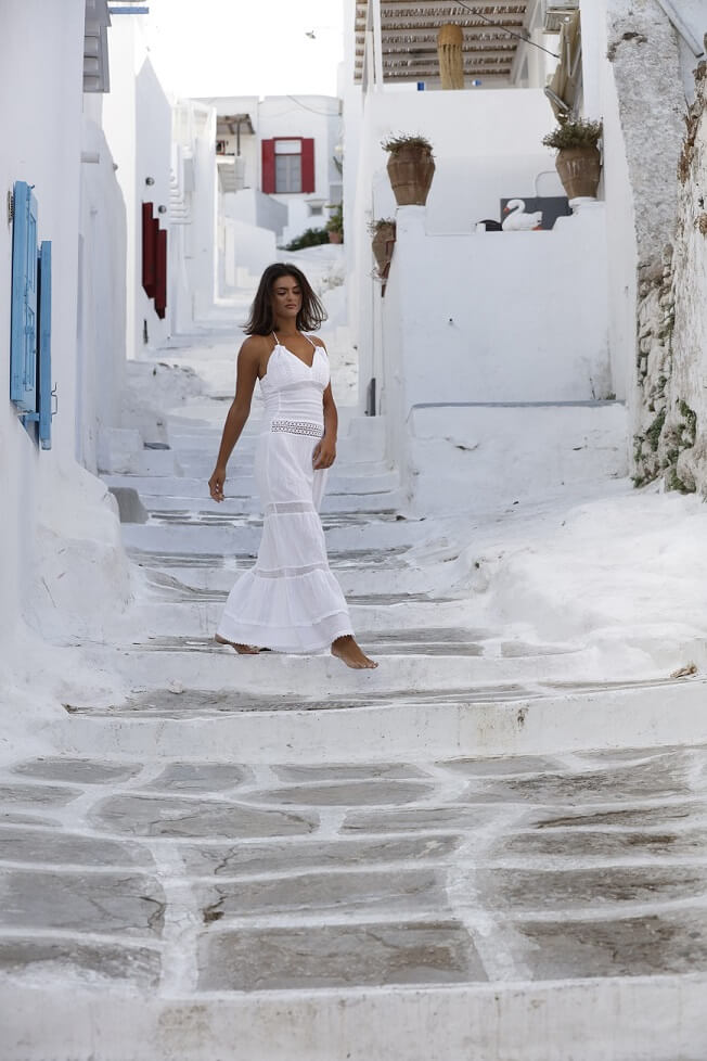 Woman in a white dress walking on a white alleyway with traditional Greek architecture.