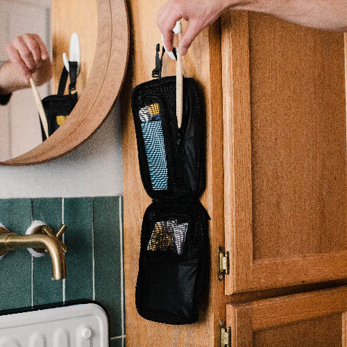 Person organizing toiletries in a black travel case on a wooden cabinet in a bathroom.