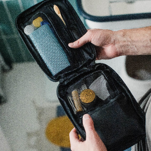 Person holding a black travel grooming kit with various items.